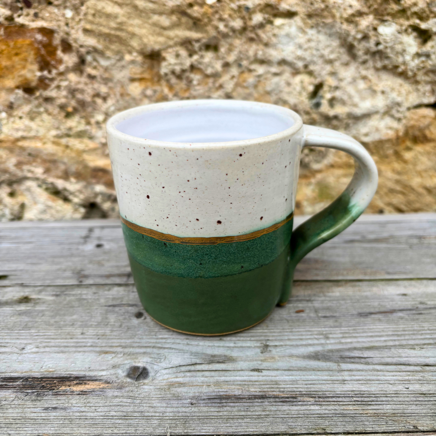 Ceramic mug with white top and green bottom on a wooden surface with stone wall background