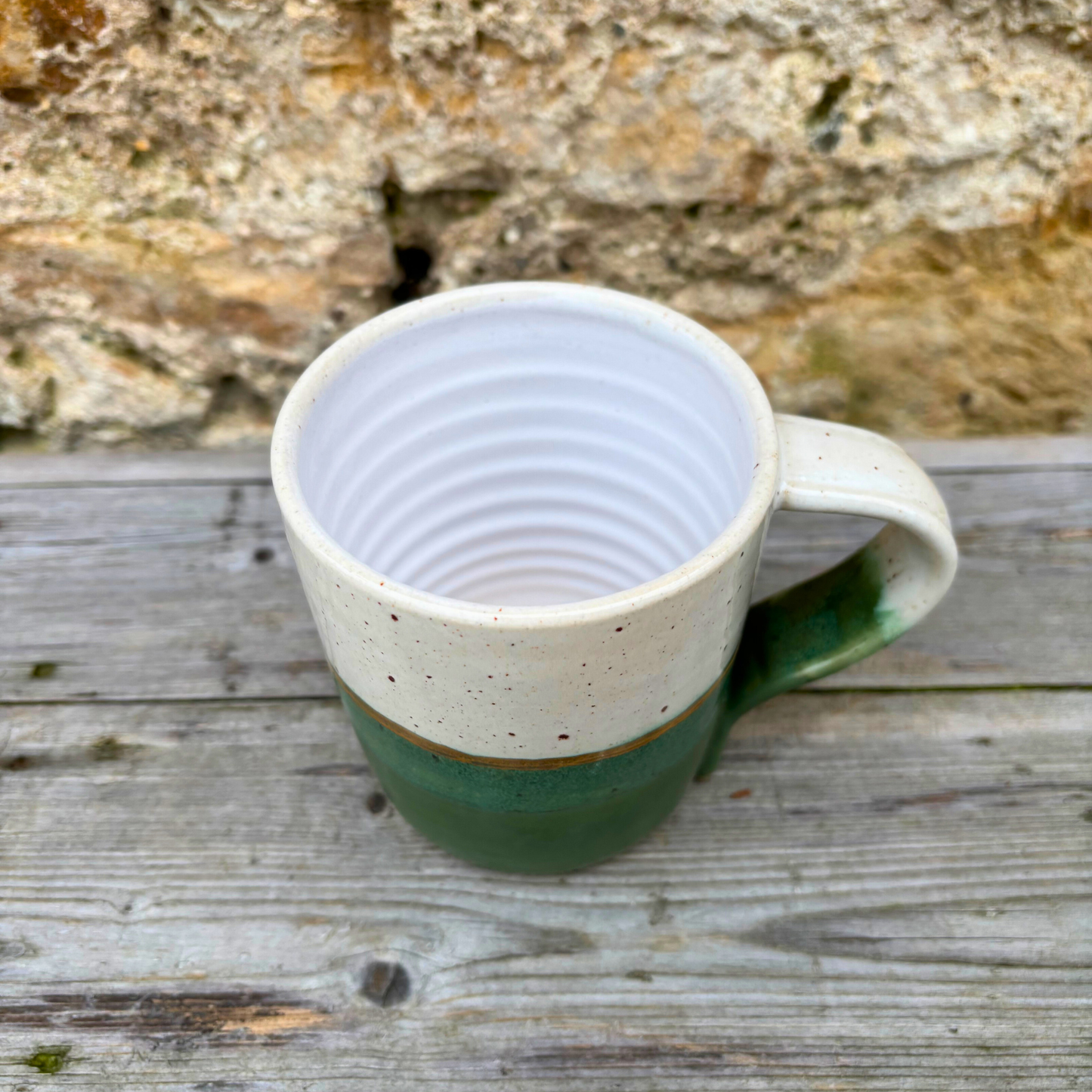 Green and white ceramic mug on a wooden surface with a stone wall background