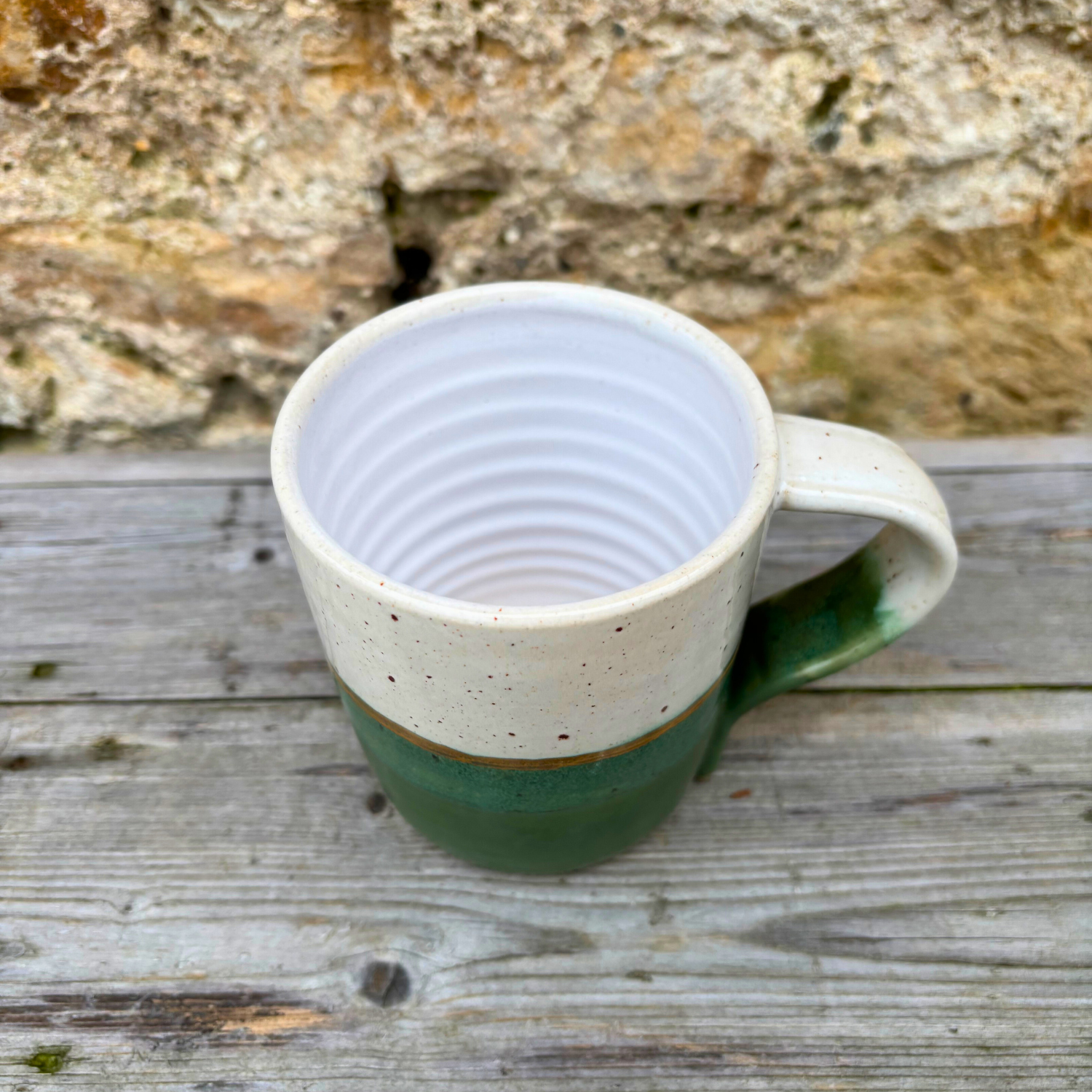 Green and white ceramic mug on a wooden surface with a stone wall background