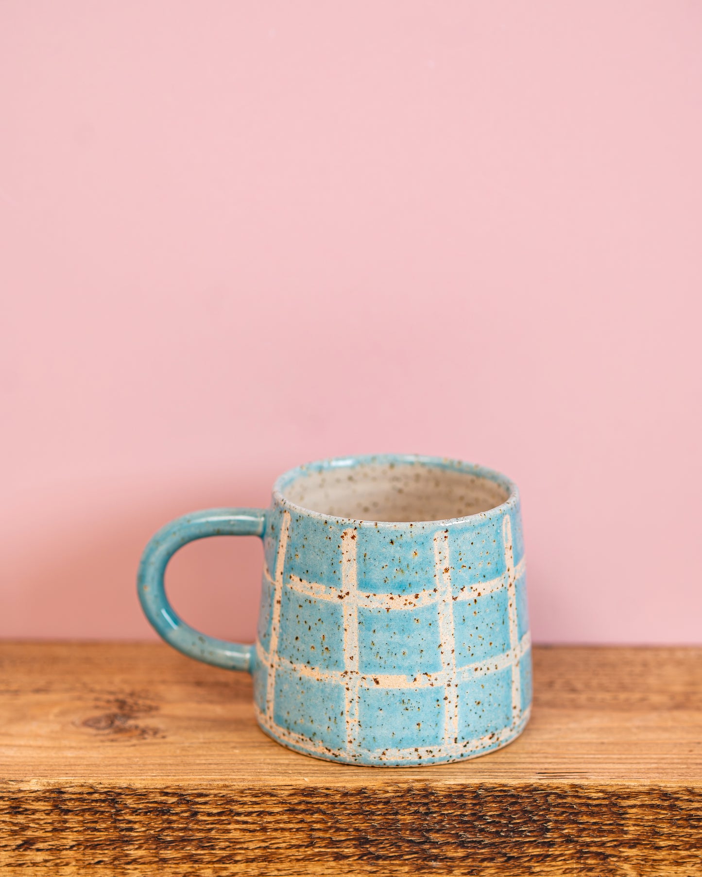 Blue ceramic mug with grid pattern on a wooden surface and pink background
