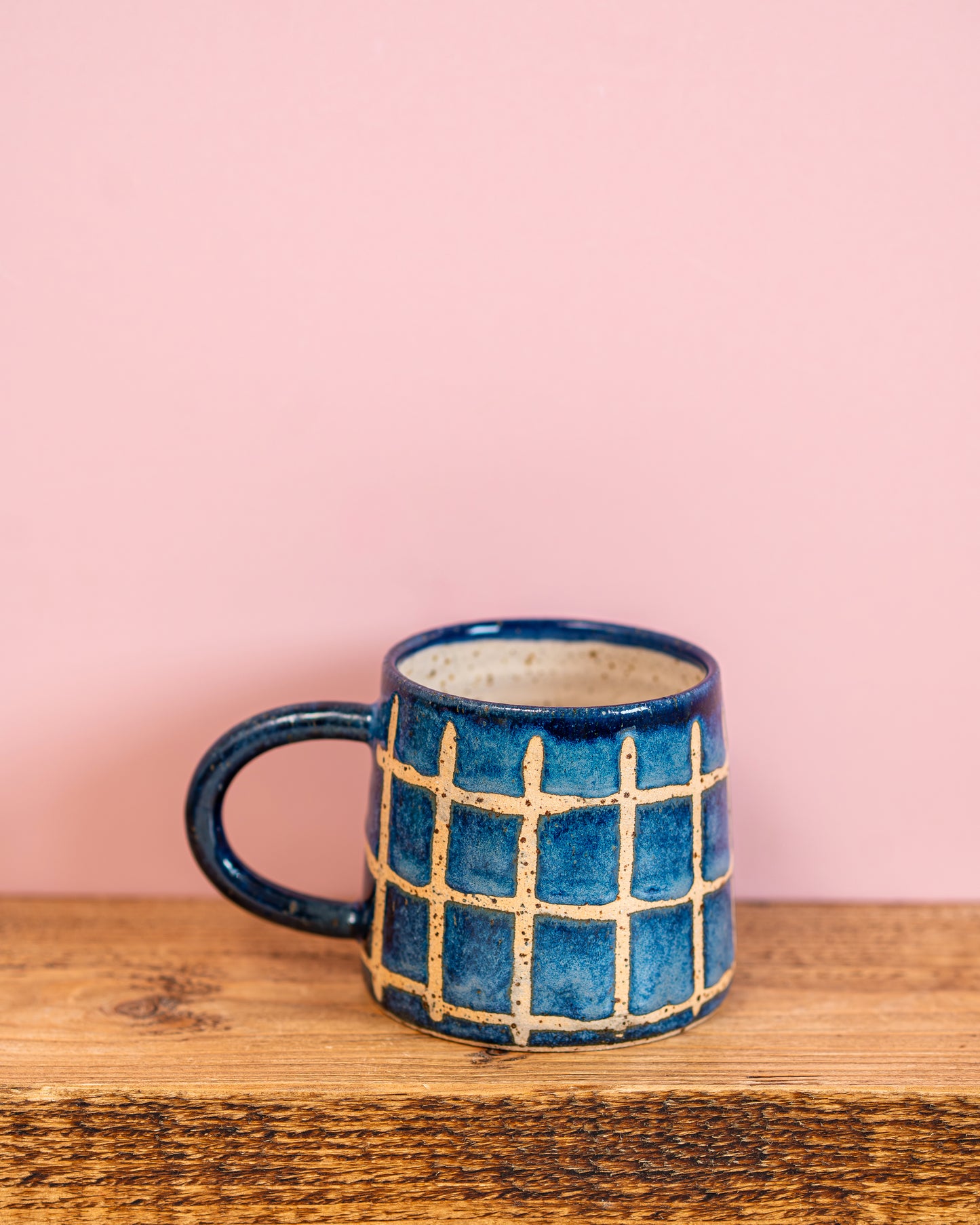 Blue ceramic mug with grid pattern on a wooden surface and pink background