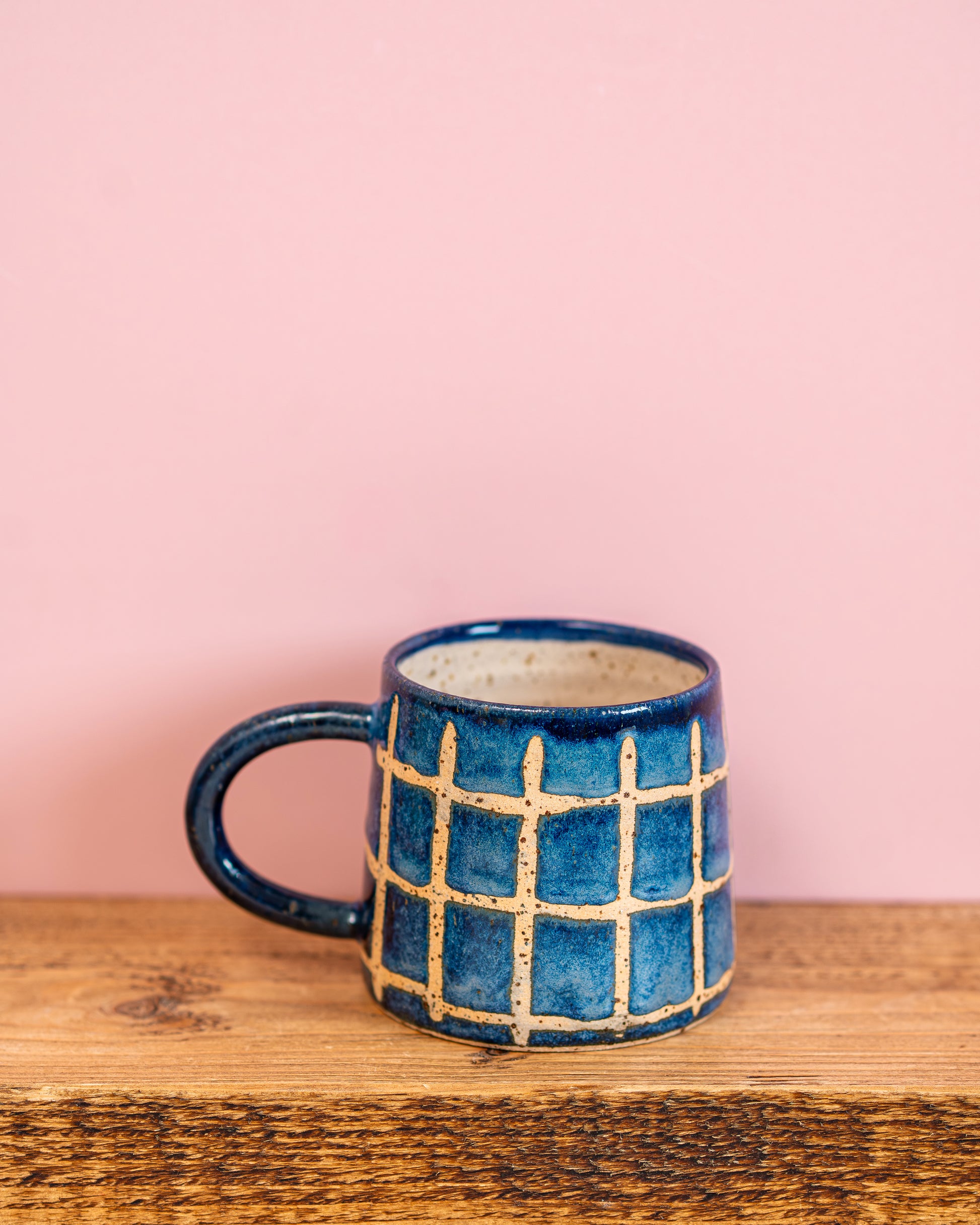Blue ceramic mug with grid pattern on a wooden surface and pink background