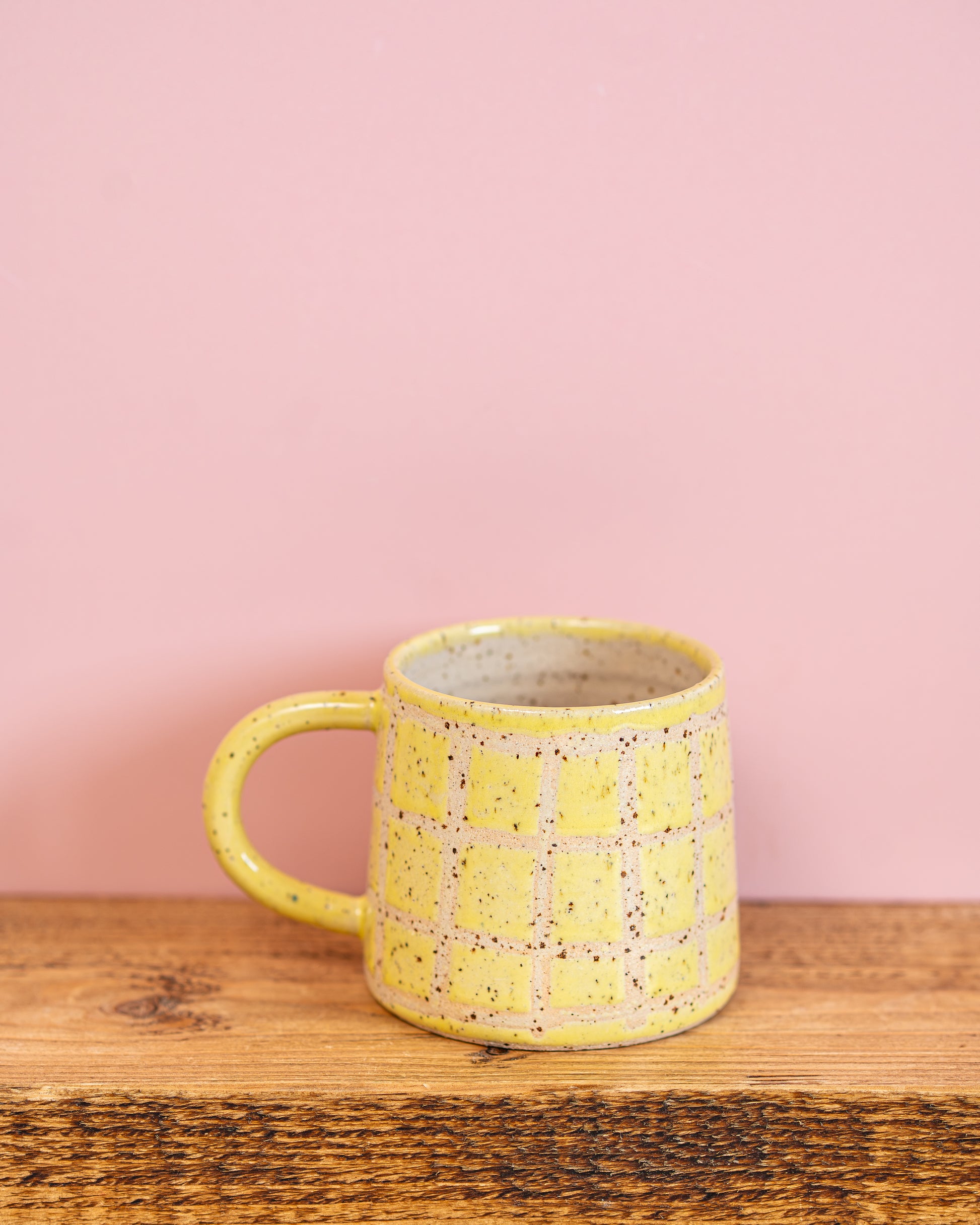 Yellow ceramic mug with speckled pattern on a wooden surface against a pink background