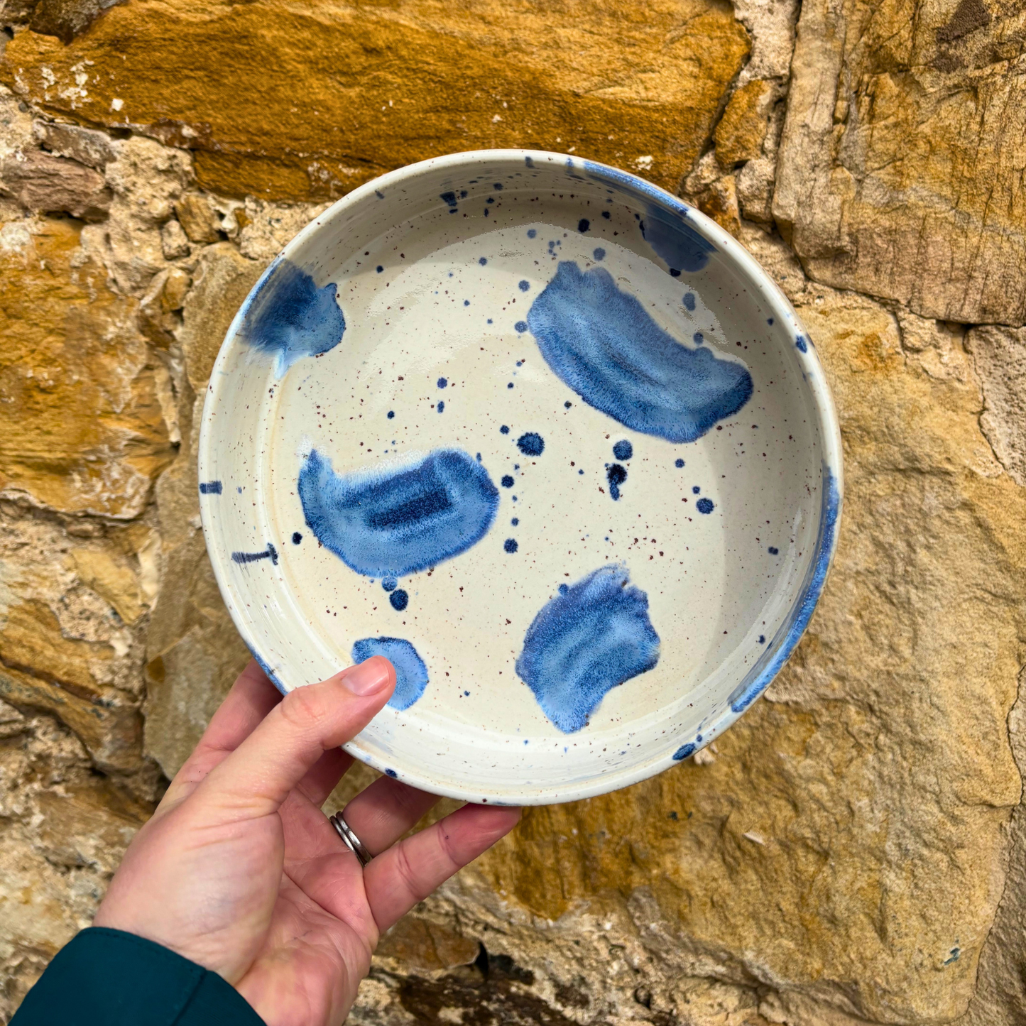 Hand holding a ceramic plate with blue abstract designs against a stone wall background
