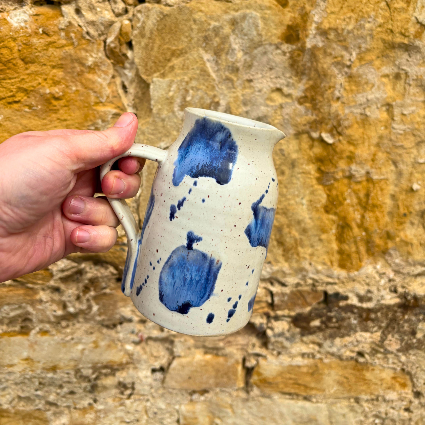 Hand holding a ceramic mug with blue speckles against a stone wall background