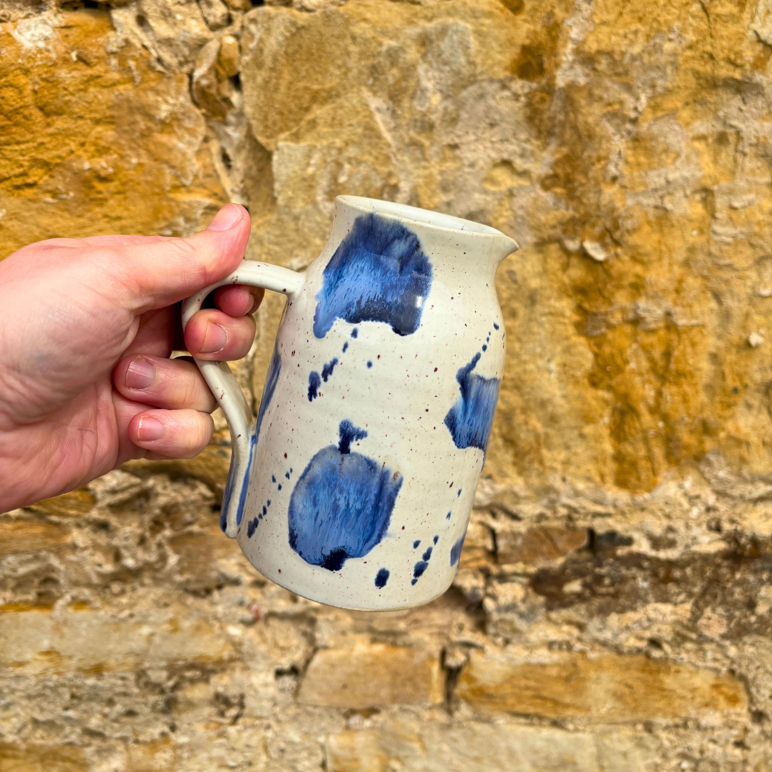 Hand holding a ceramic mug with blue speckles against a stone wall background
