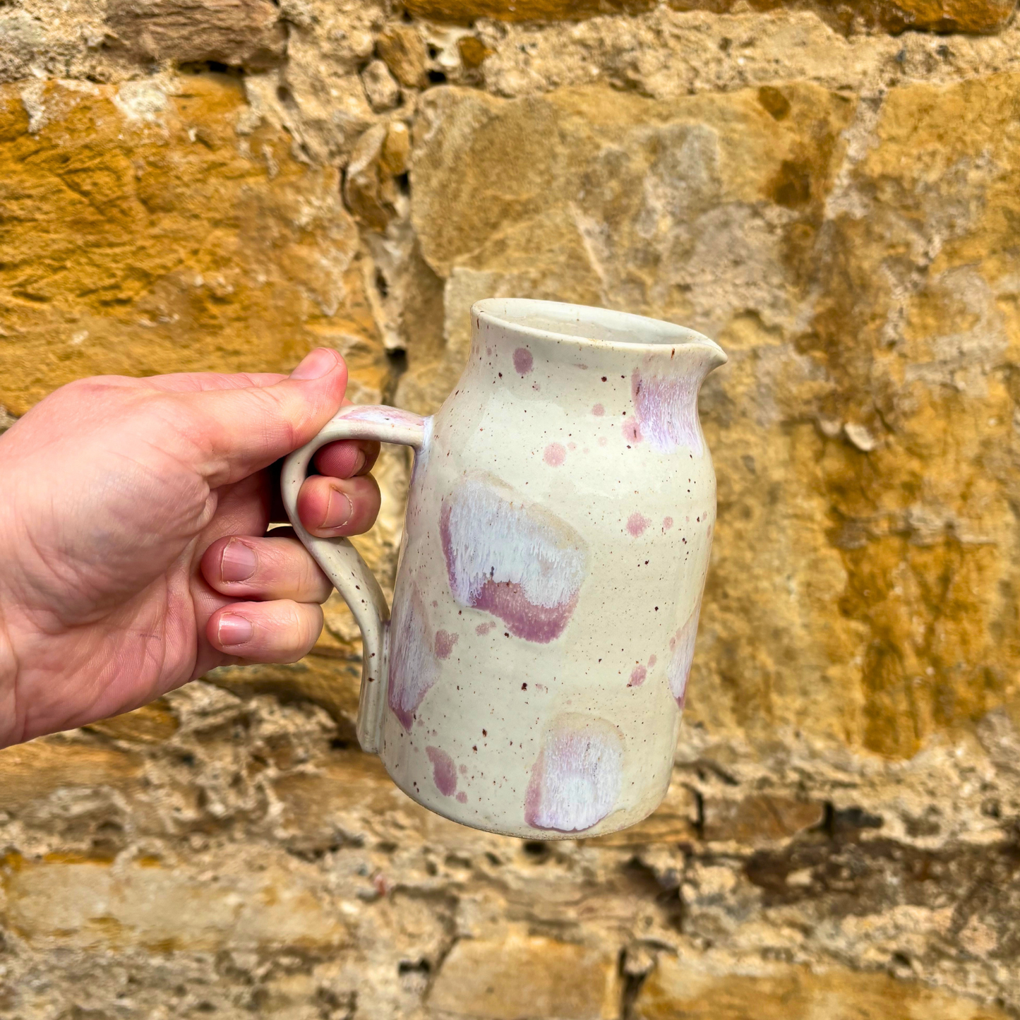 Hand holding a ceramic mug with pink speckles against a stone wall background