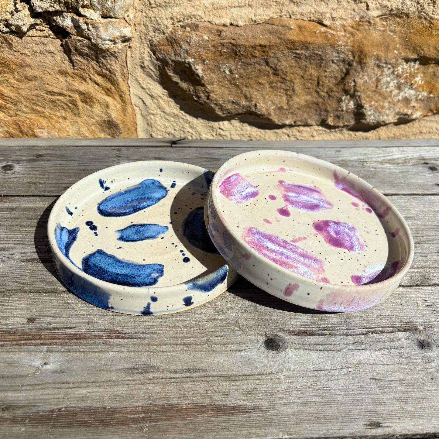 Two ceramic trinket dishes with abstract designs on a wooden surface with a rock background
