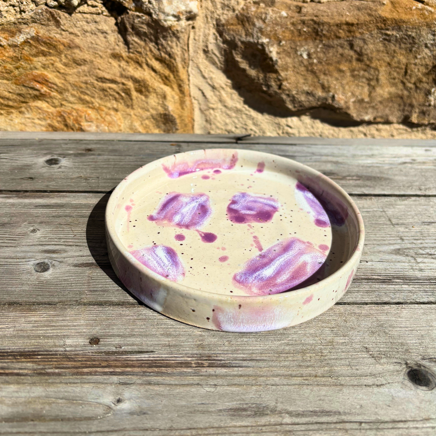 Round ceramic dish with purple abstract design on a wooden surface with stone background
