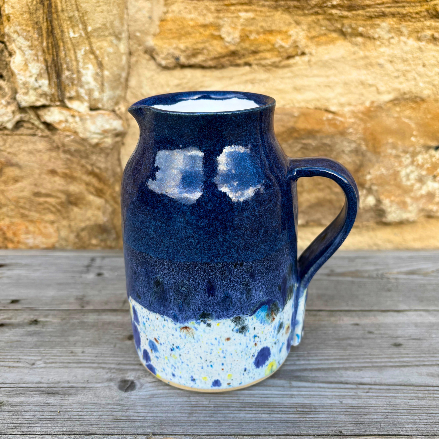 Blue ceramic pitcher with speckled design on a wooden surface with stone wall background