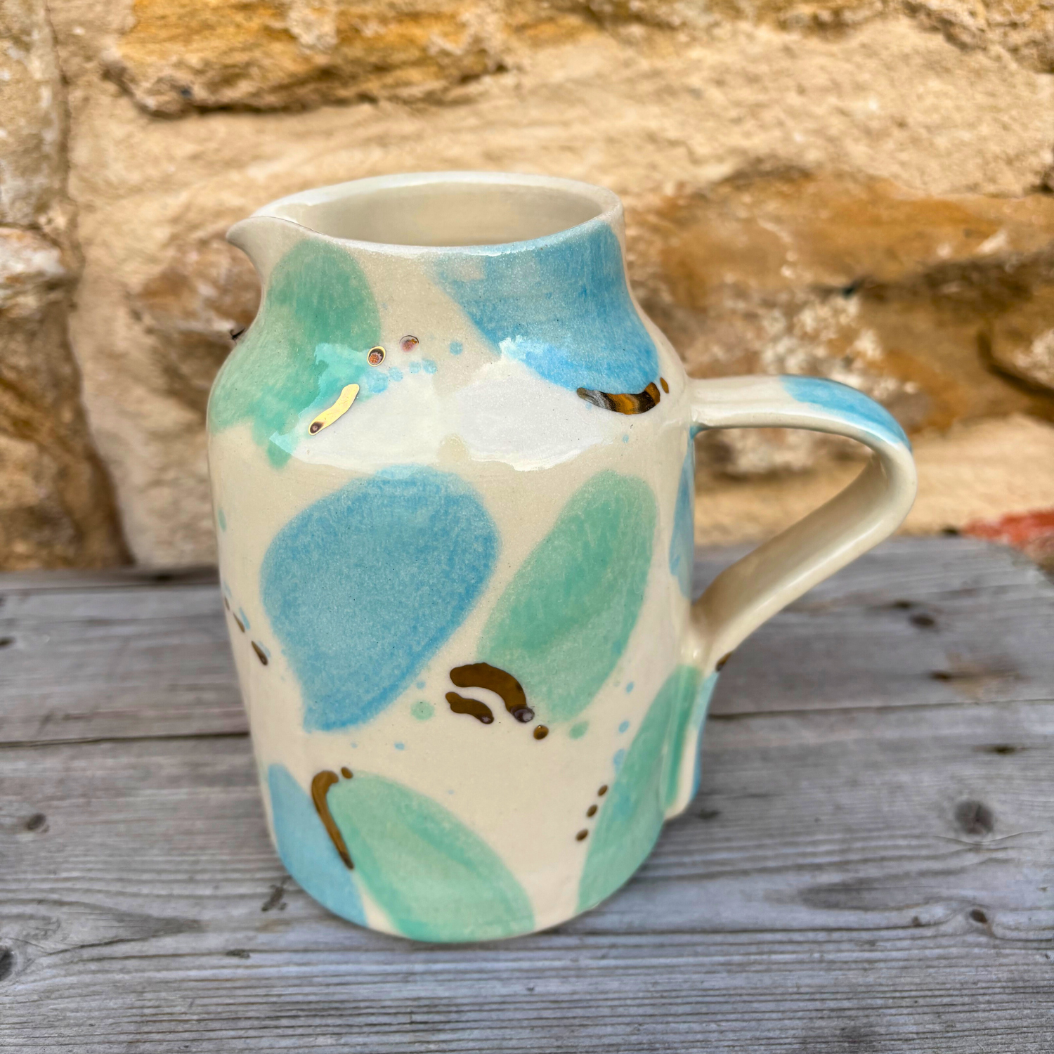 Ceramic jug with blue and green abstract design on a wooden surface