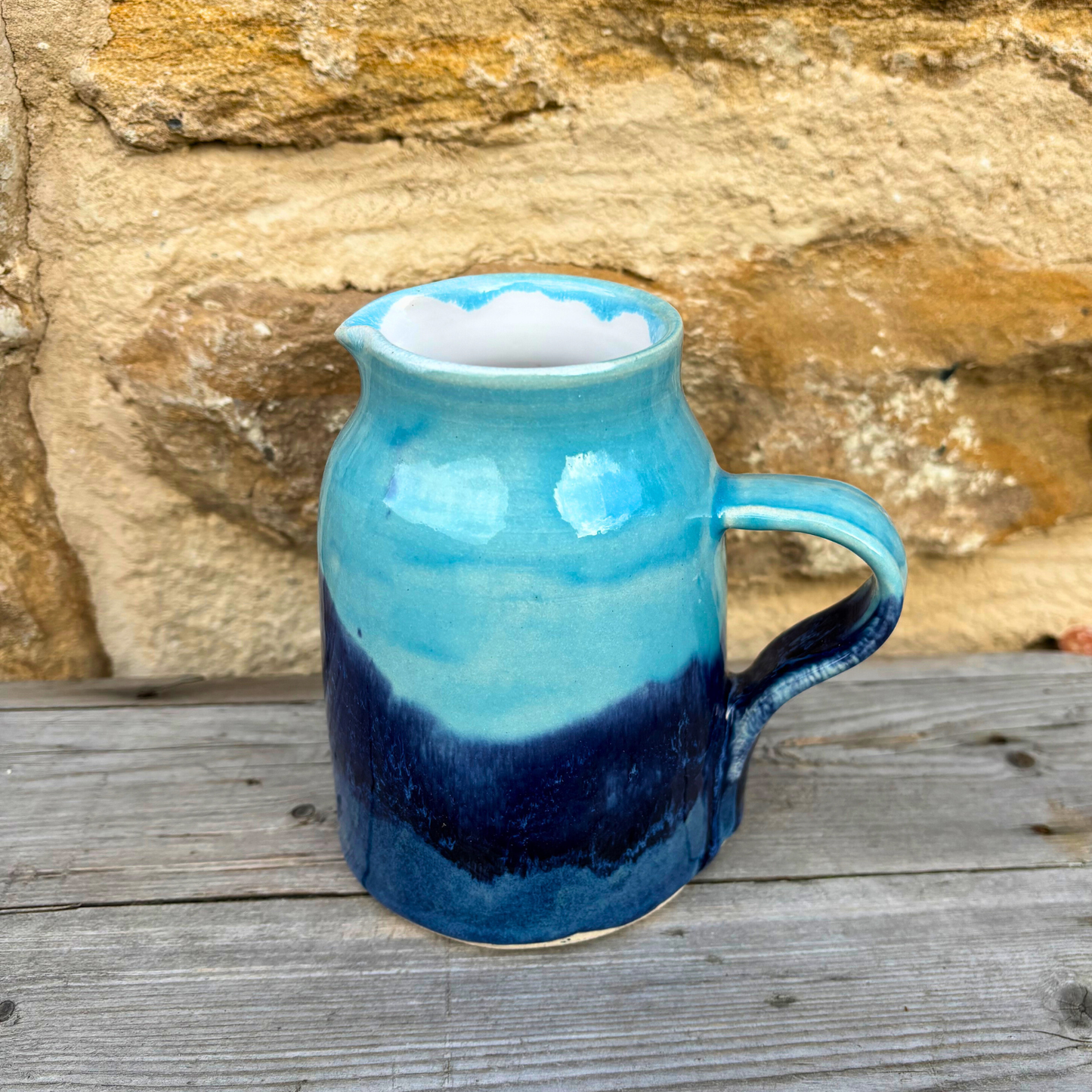 Blue and navy ceramic pitcher on a wooden surface with a stone wall background