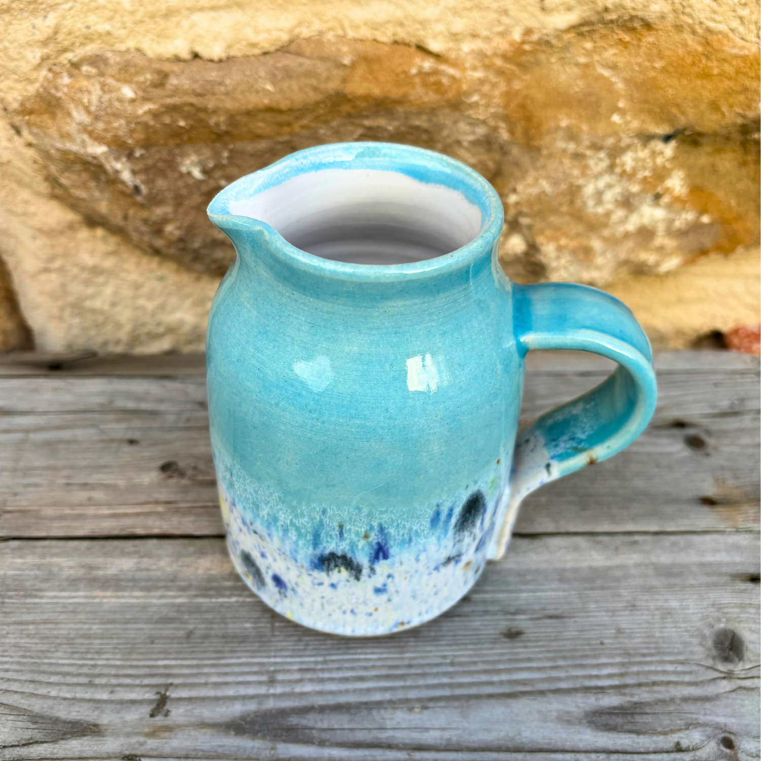 Blue ceramic pitcher on a wooden surface with a stone background