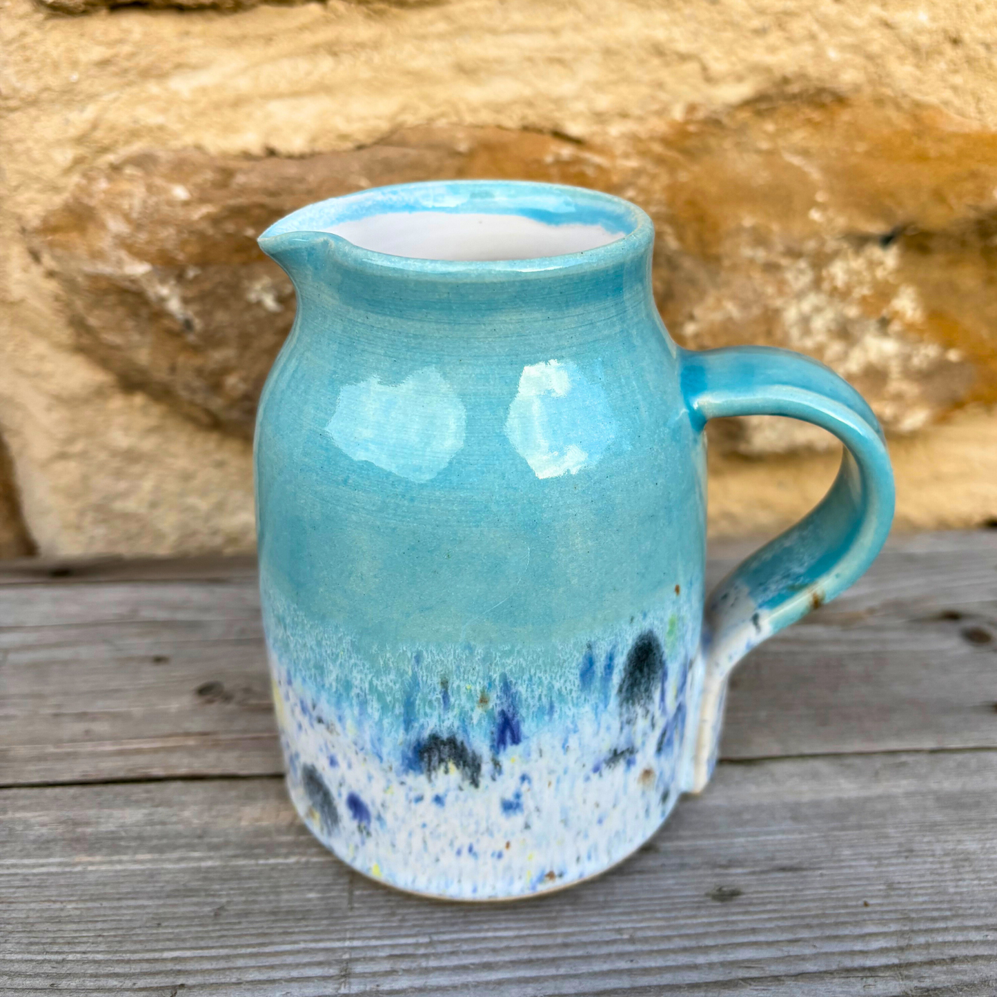 Blue ceramic pitcher with speckled design on a wooden surface