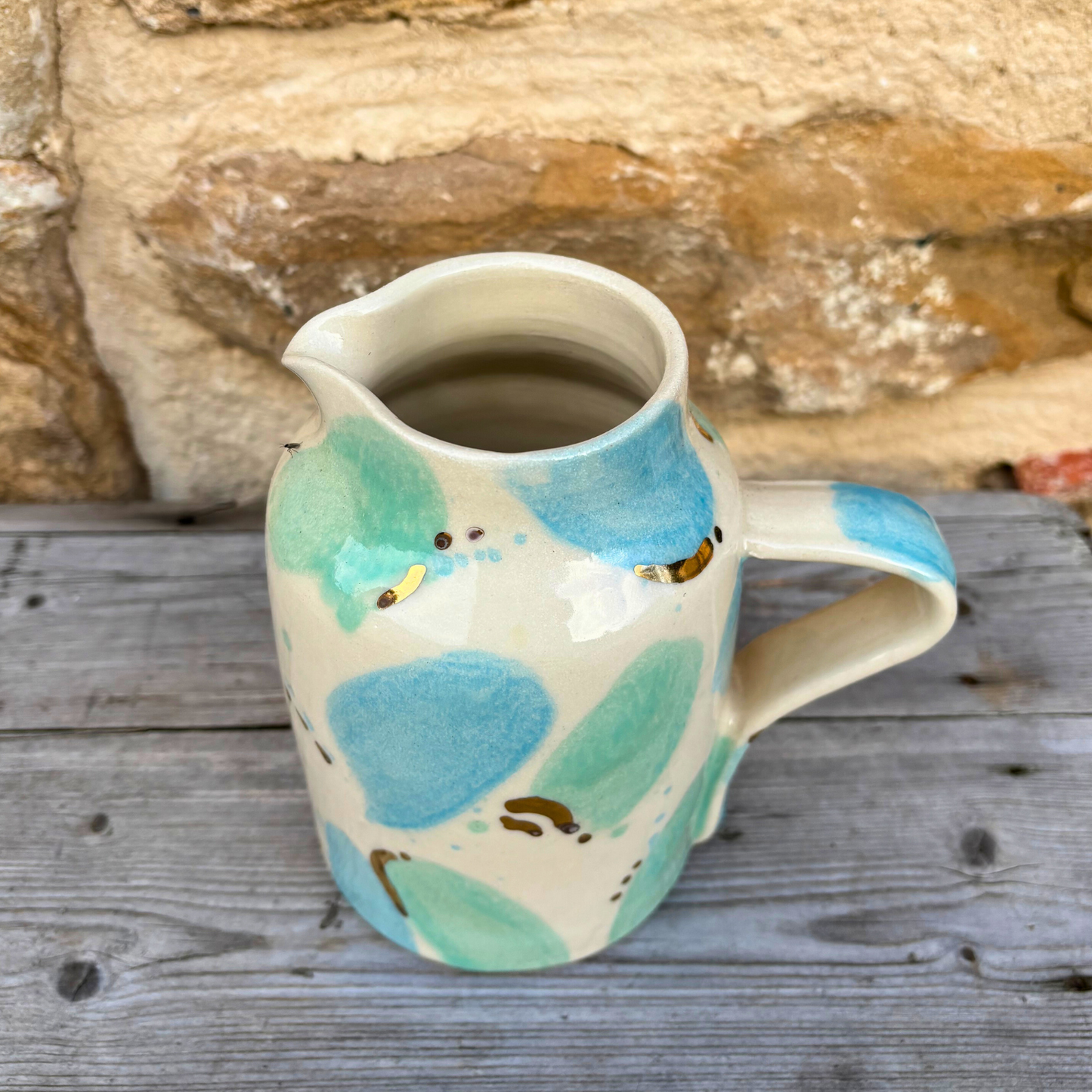 Ceramic pitcher with colourful design on a wooden surface