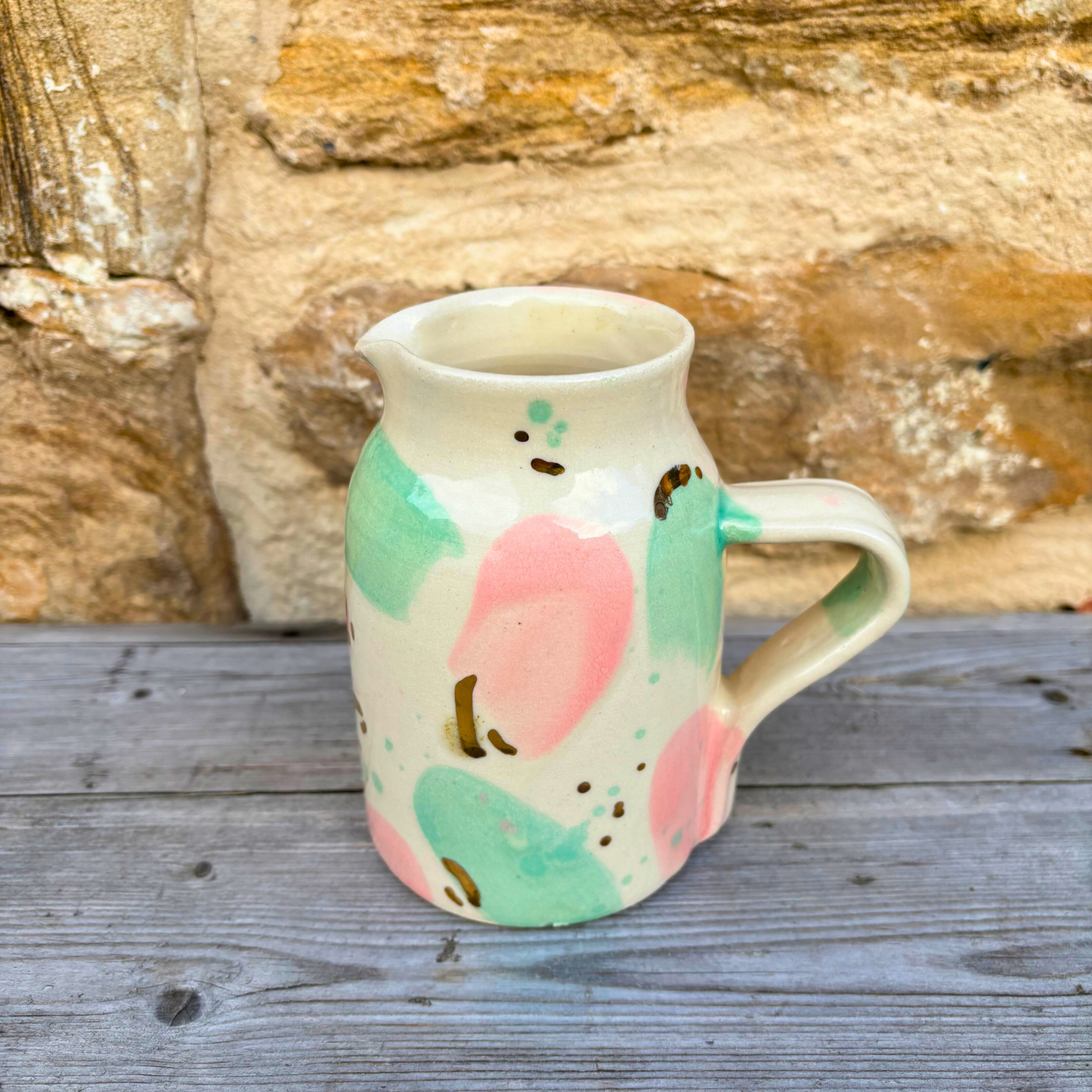 Ceramic pitcher with pink and green design on a wooden surface