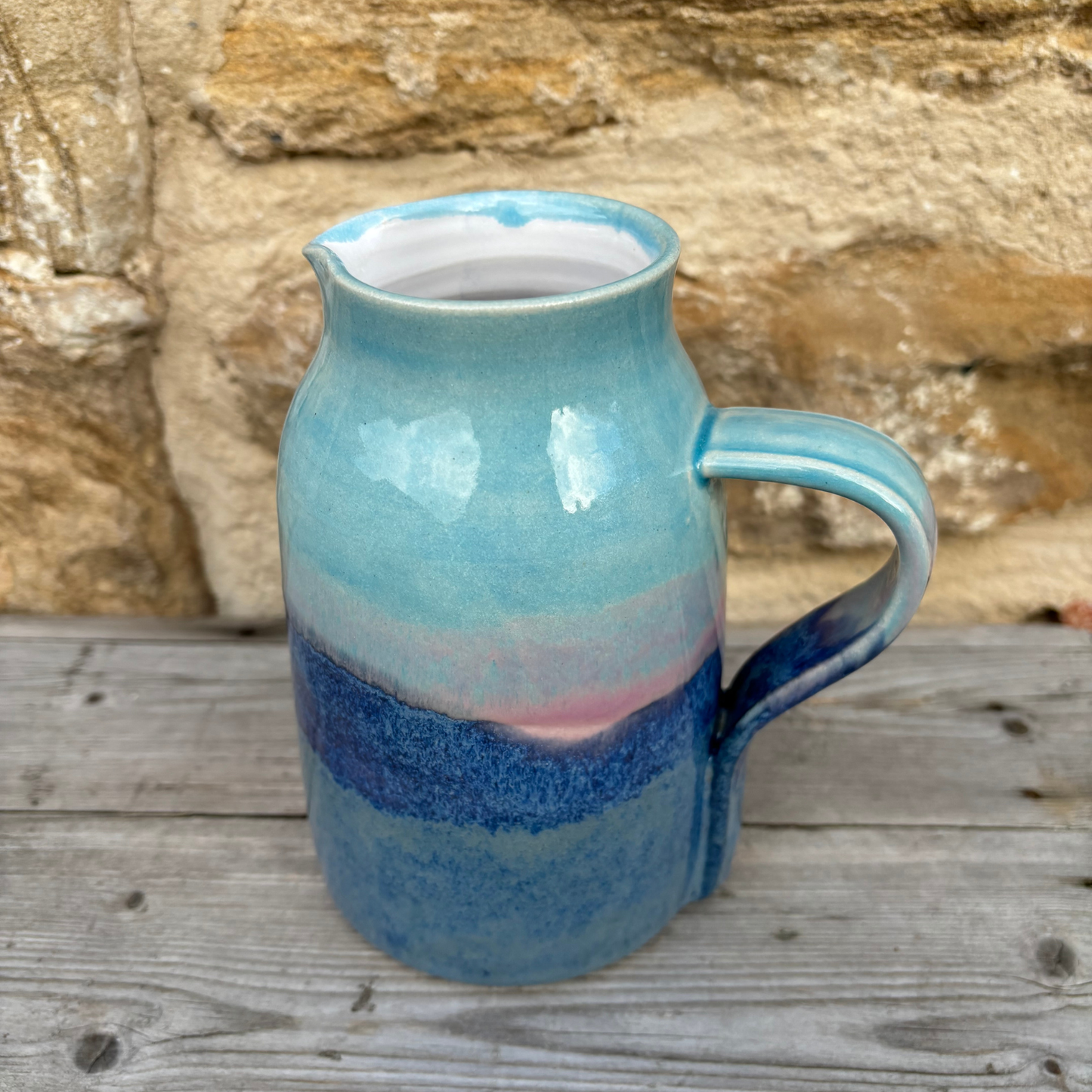 Blue ceramic pitcher with a textured surface on a wooden surface with a stone wall background