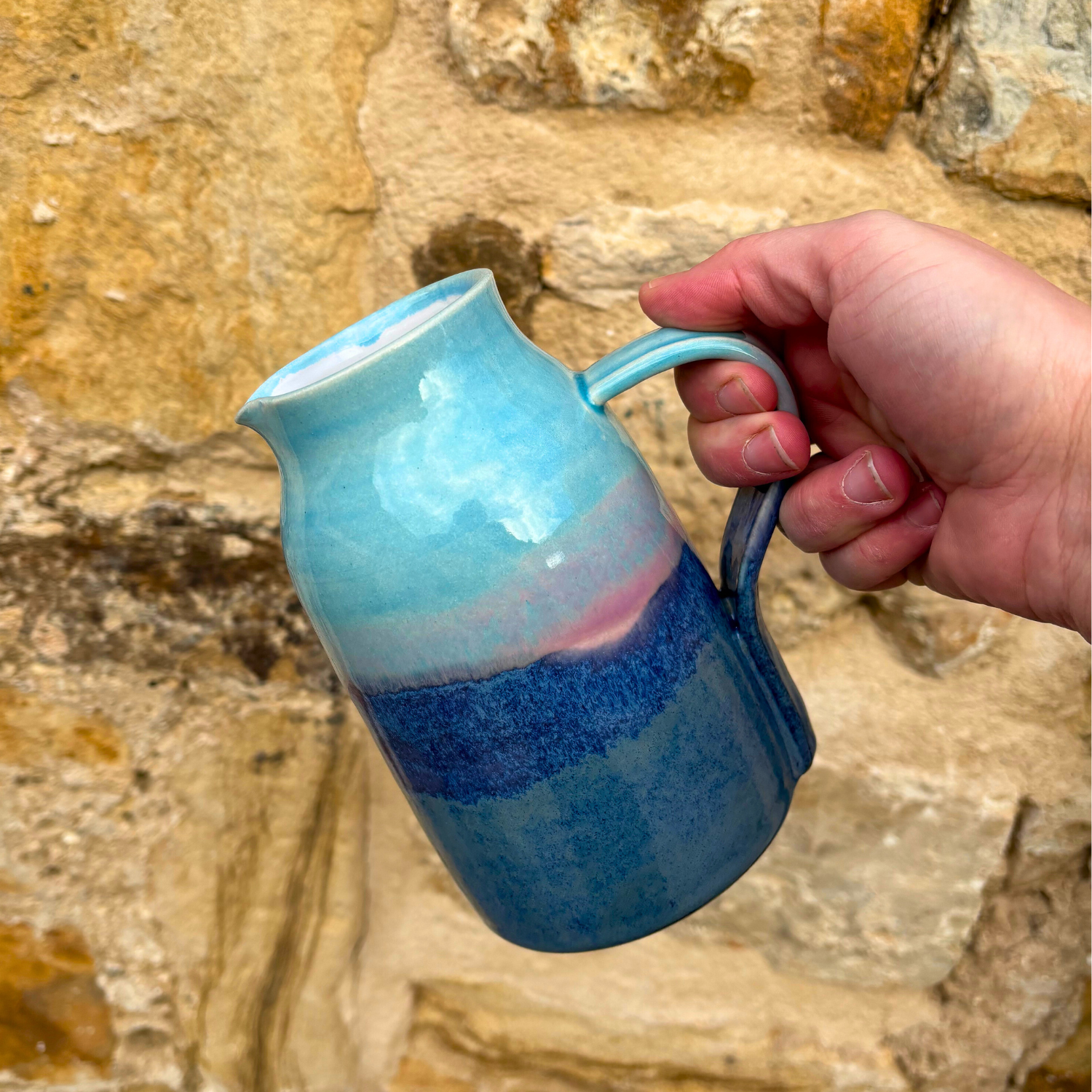 Hand holding a blue and pink ceramic mug against a stone wall background