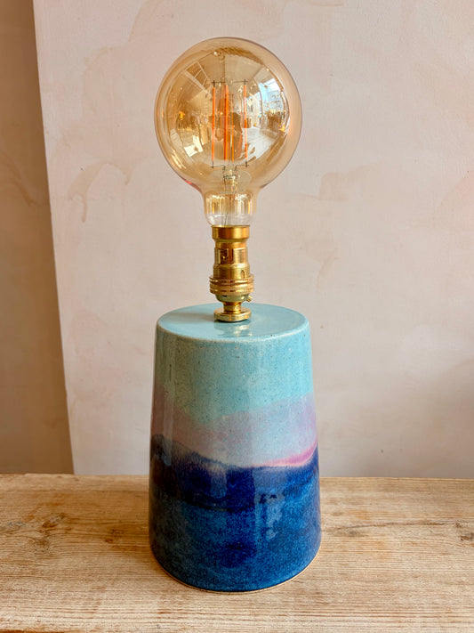 Table lamp with a blue and pink gradient base and a vintage-style bulb on a wooden surface.