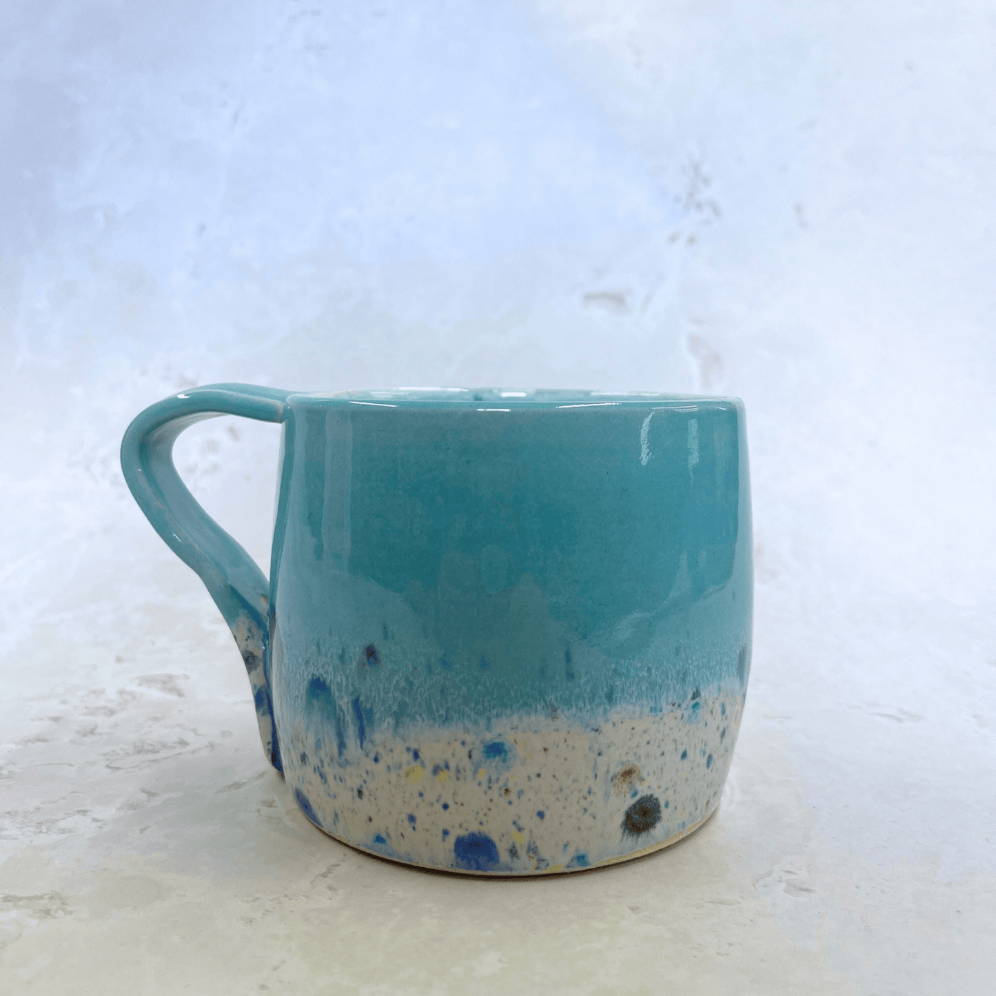 Ella Fletcher Designs Handmade Pottery Large Round Mug in Pale Blue Shoreline Design, solid blue with speckled multicolour design on a round handmade mug
