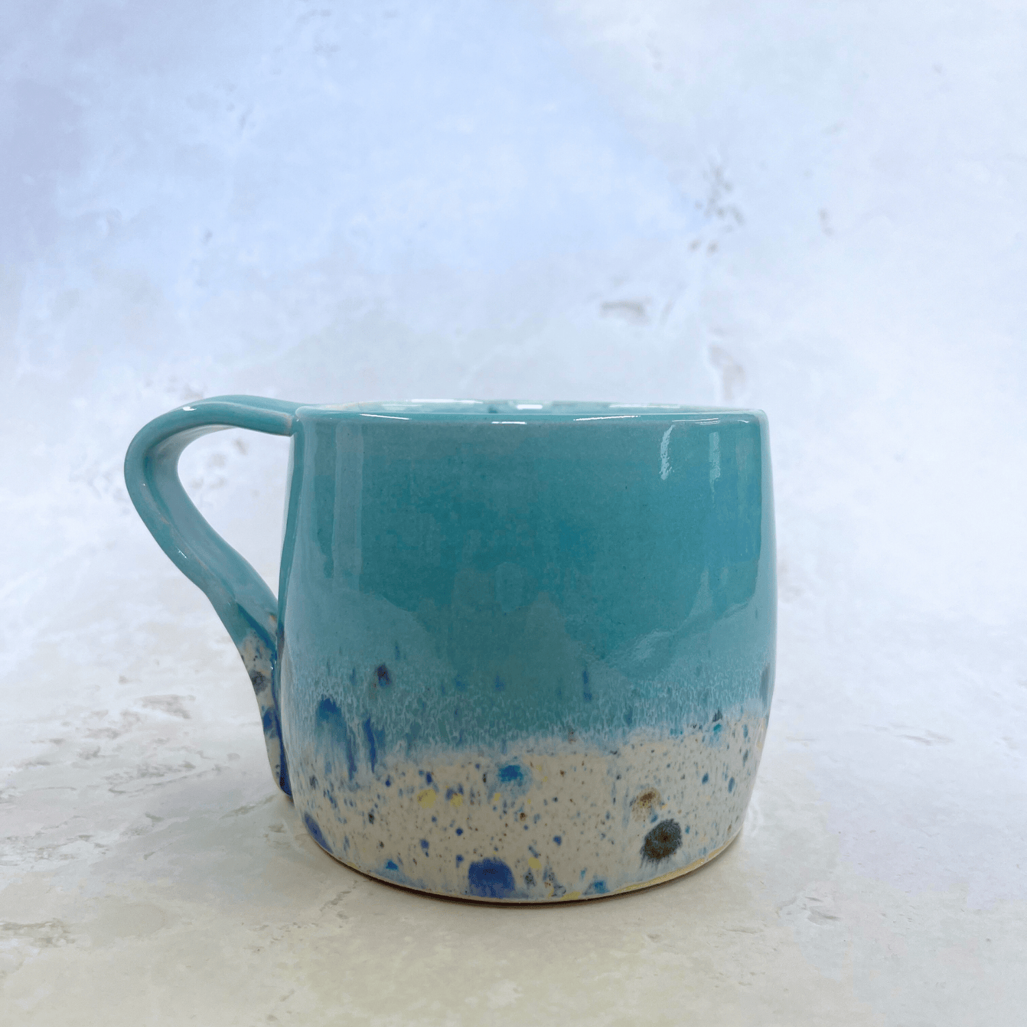 Ella Fletcher Designs Handmade Pottery Large Round Mug in Pale Blue Shoreline Design, solid blue with speckled multicolour design on a round handmade mug