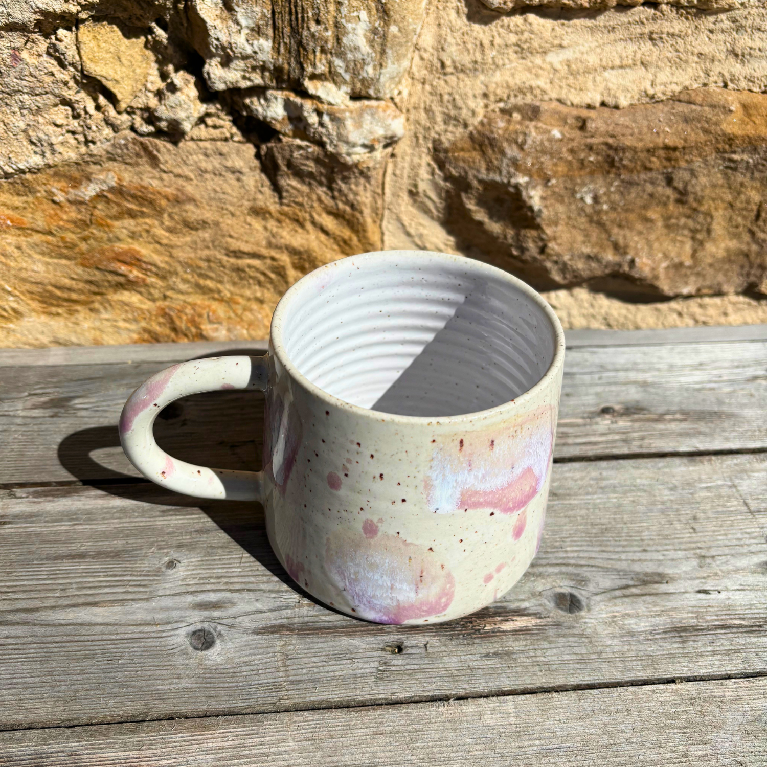 Ceramic mug with speckled design on a wooden surface with stone wall background