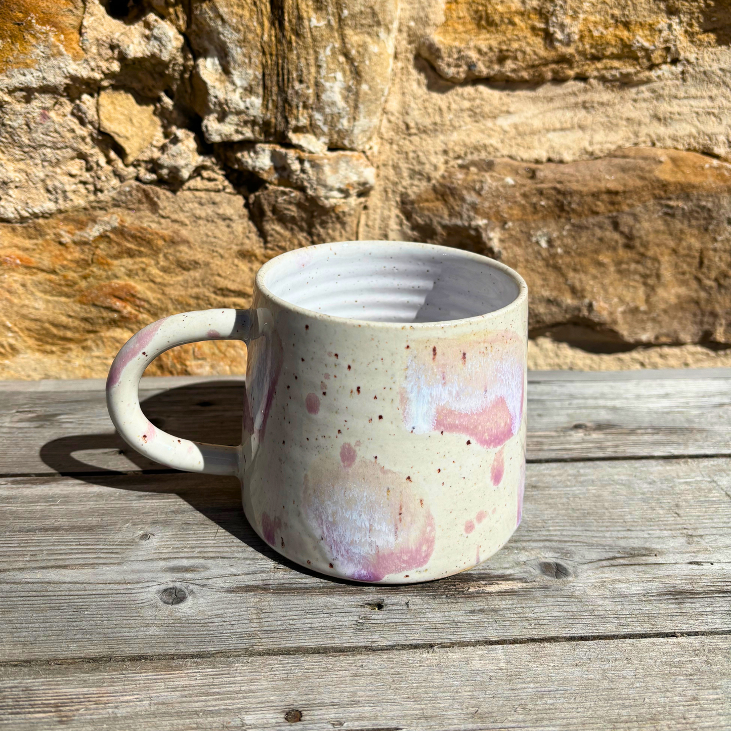 Speckled ceramic mug on a wooden surface with a stone wall background