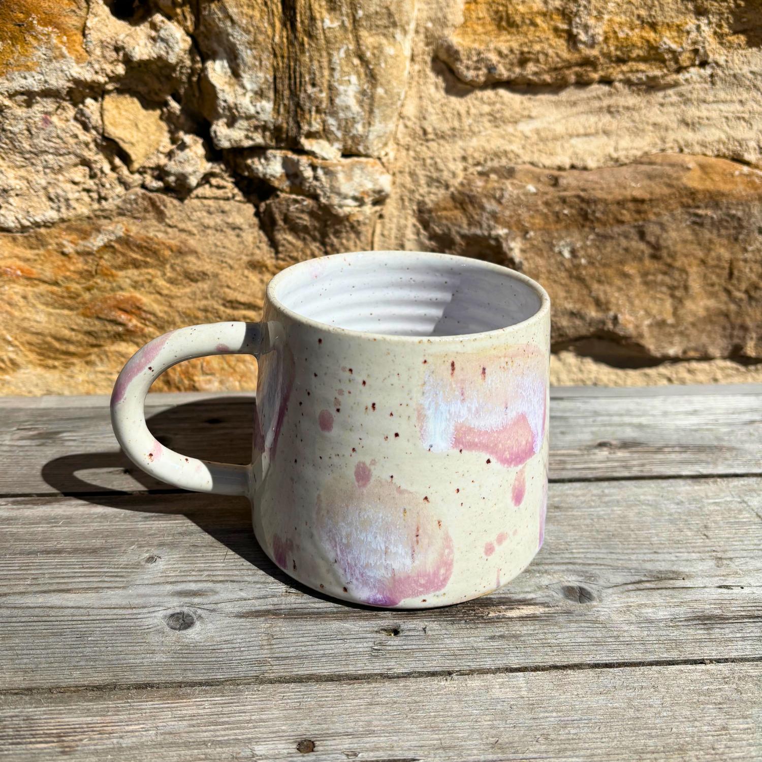 Speckled ceramic mug on a wooden surface with a stone wall background