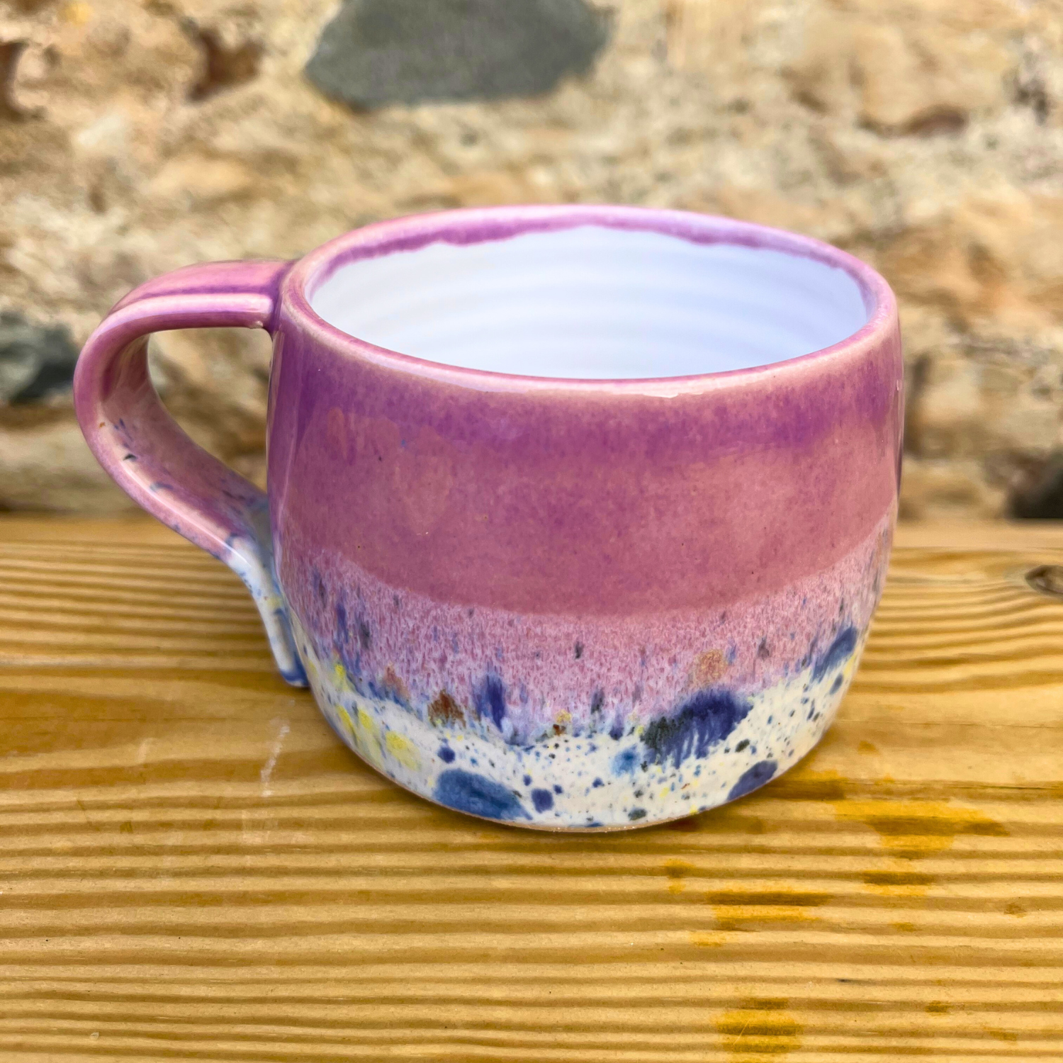 Multicolored ceramic mug on a wooden surface with a natural stone background