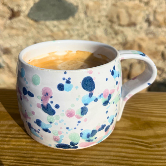 Mug with colorful dot pattern containing a beverage on a wooden surface with a stone wall background