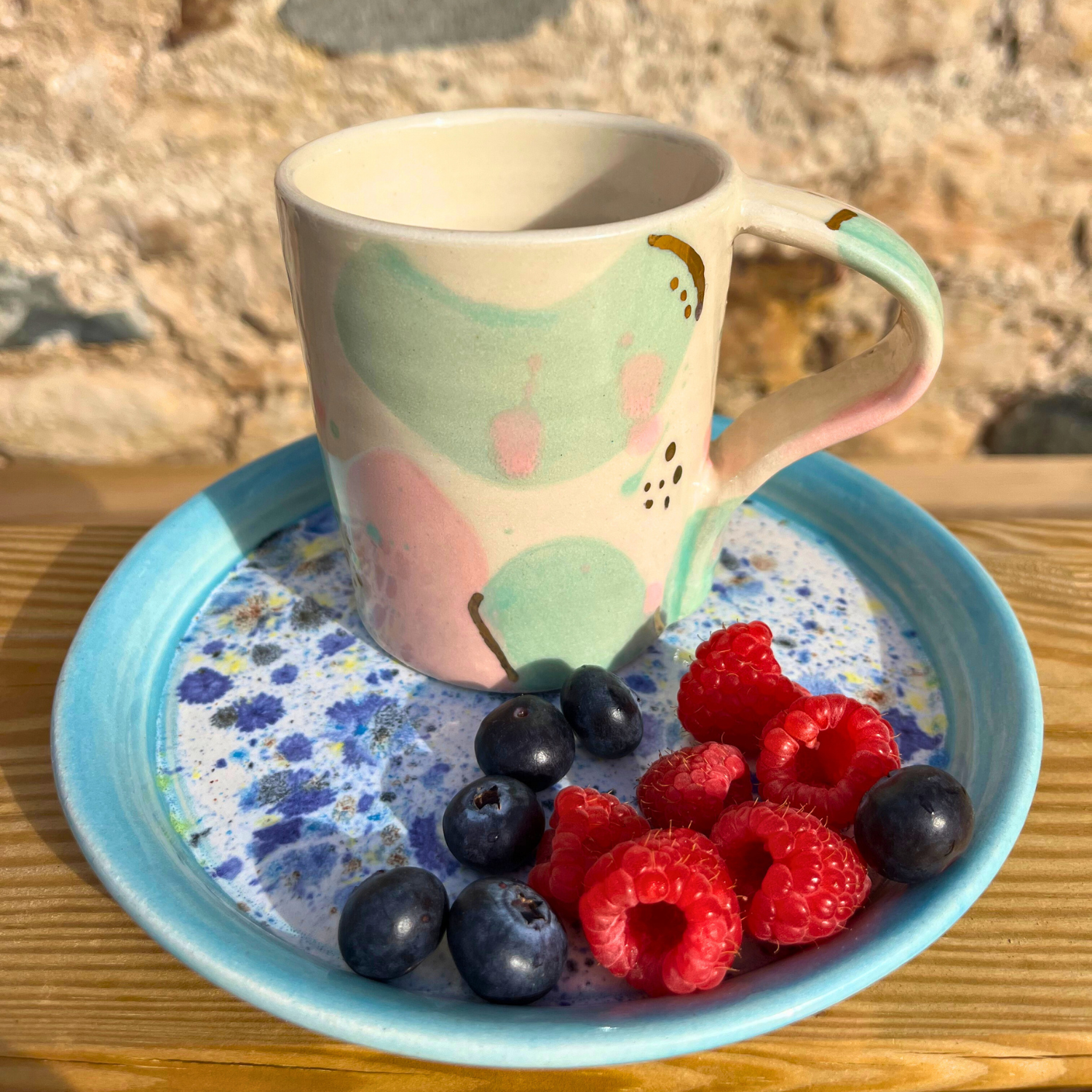 Mug with colorful design on a blue plate with berries on a wooden surface