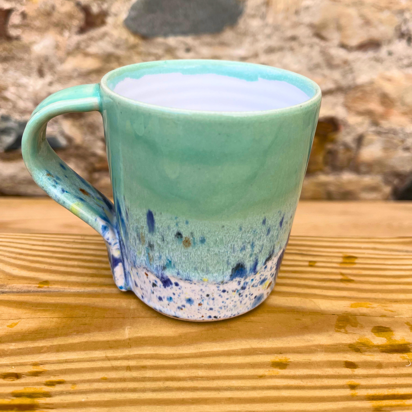 Green ceramic mug with speckled design on a wooden surface
