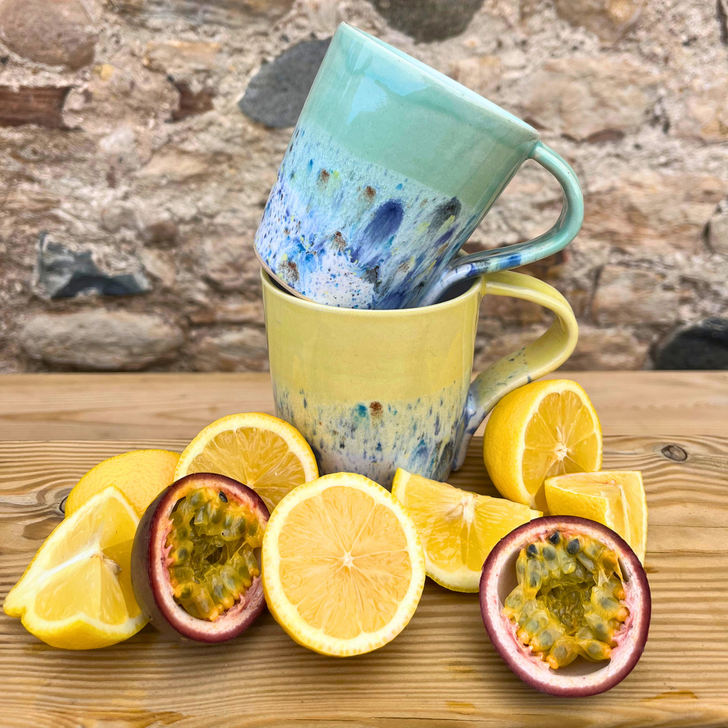 Two ceramic mugs stacked with lemons and passion fruits on a wooden surface.