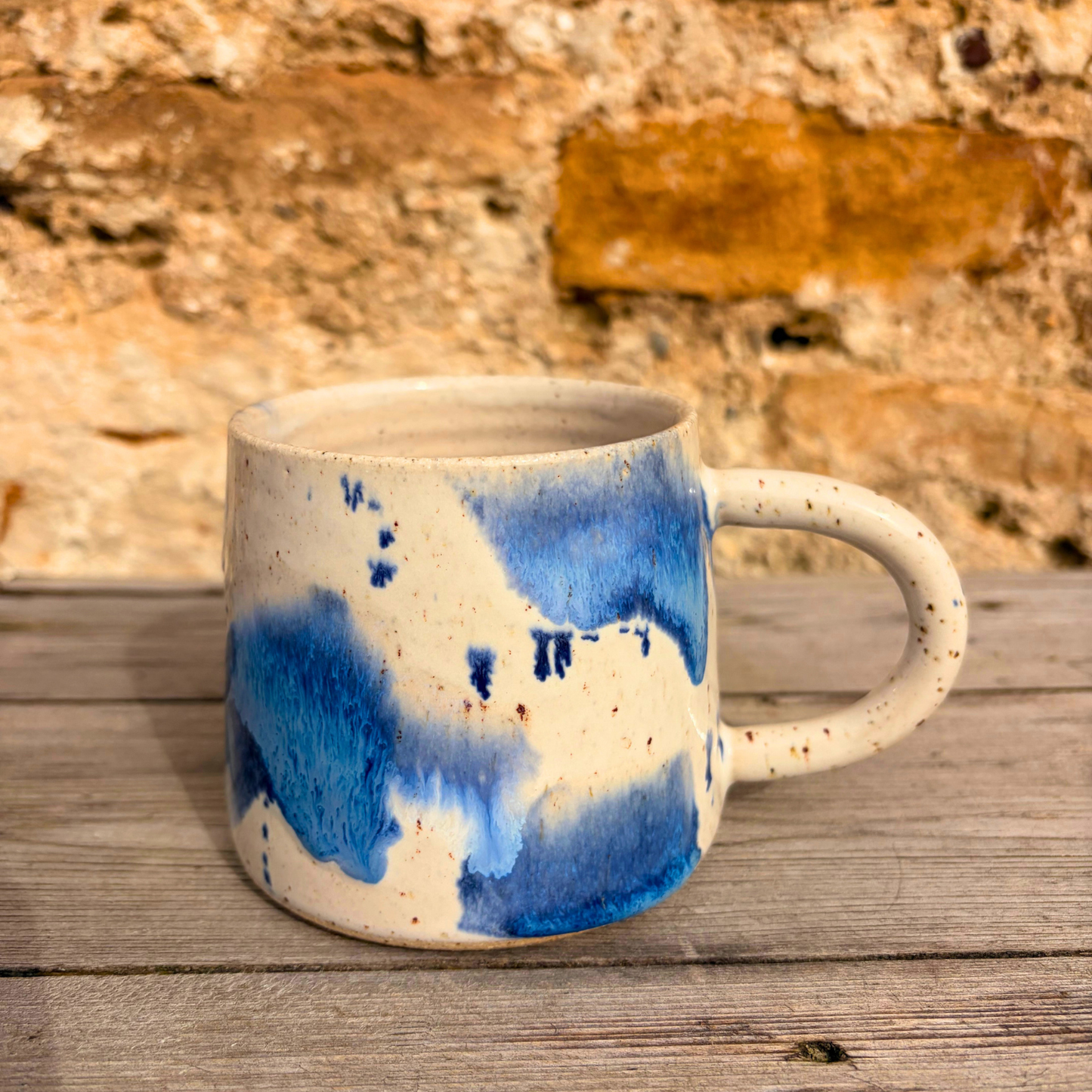 Ceramic mug with blue and white design on a wooden surface with stone wall background