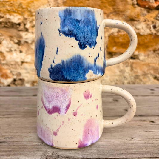 Two ceramic mugs with abstract blue and purple designs on a wooden surface.