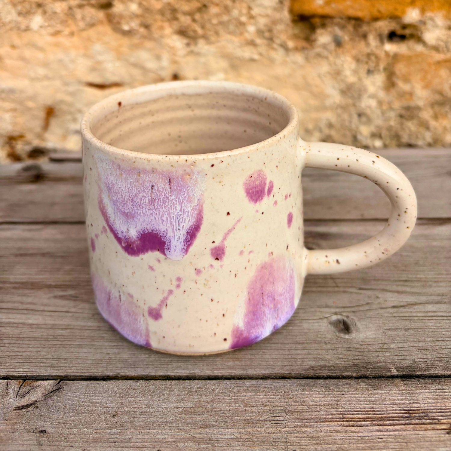 Speckled ceramic mug with purple and pink patterns on a wooden surface.