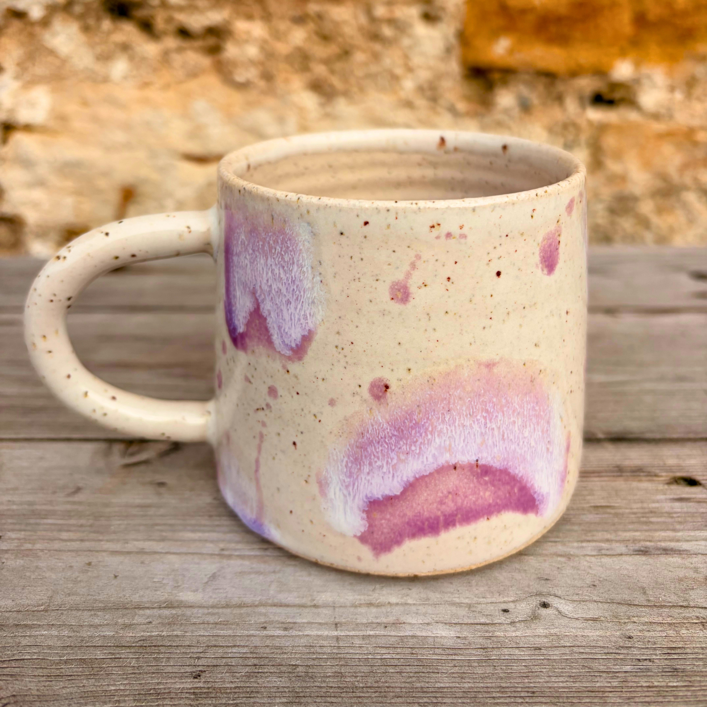 Speckled ceramic mug with purple and pink glaze on a wooden surface