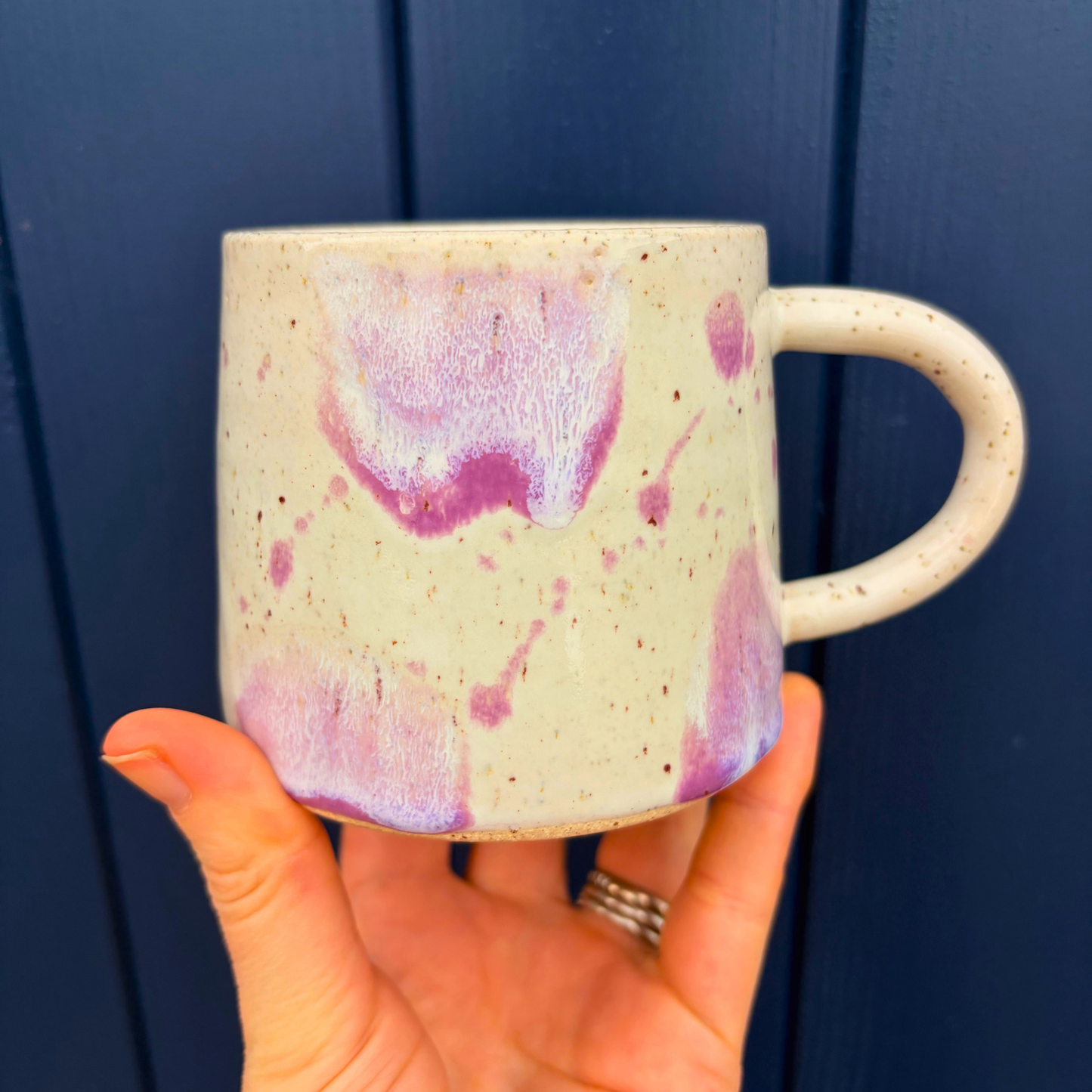 Hand holding a ceramic mug with pink speckled design against a blue wooden background
