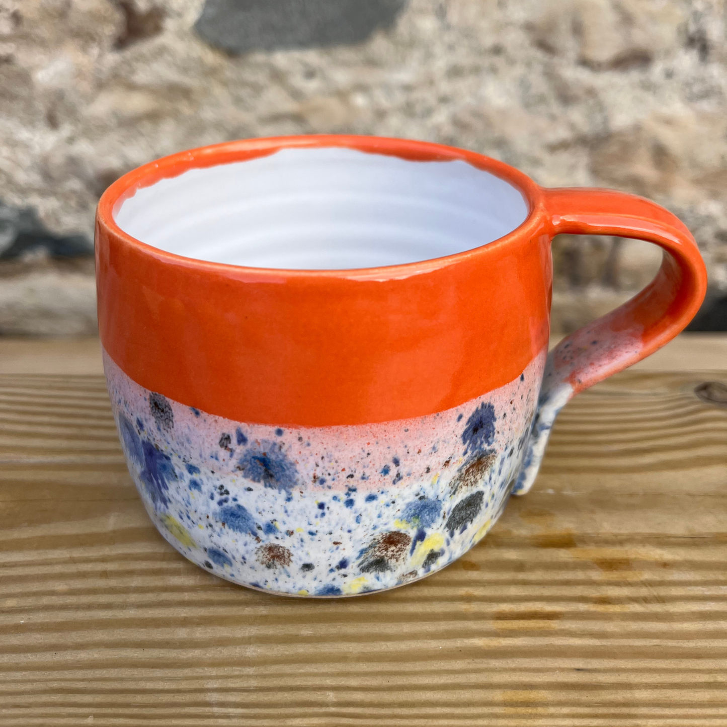 Speckled mug with orange rim and handle on a wooden surface