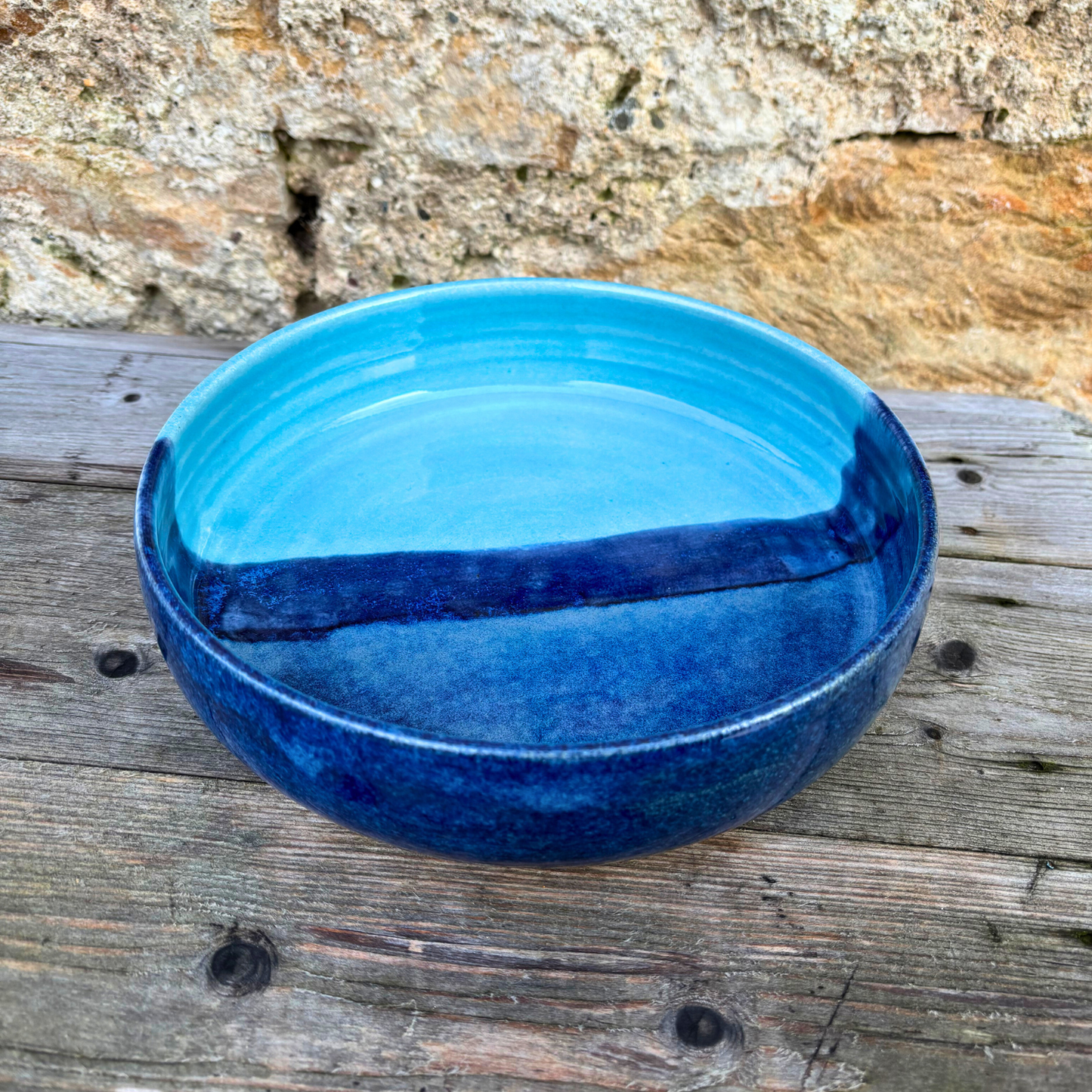 Blue ceramic bowl on a wooden surface with a stone wall background