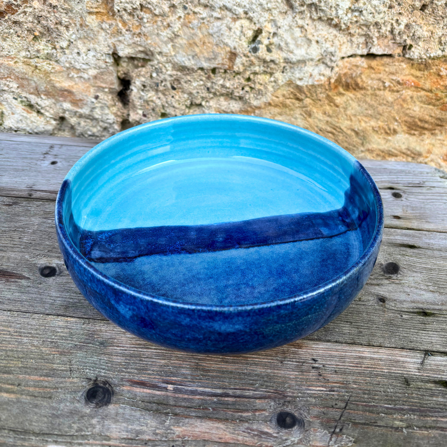 Blue ceramic bowl on a wooden surface with a stone wall background