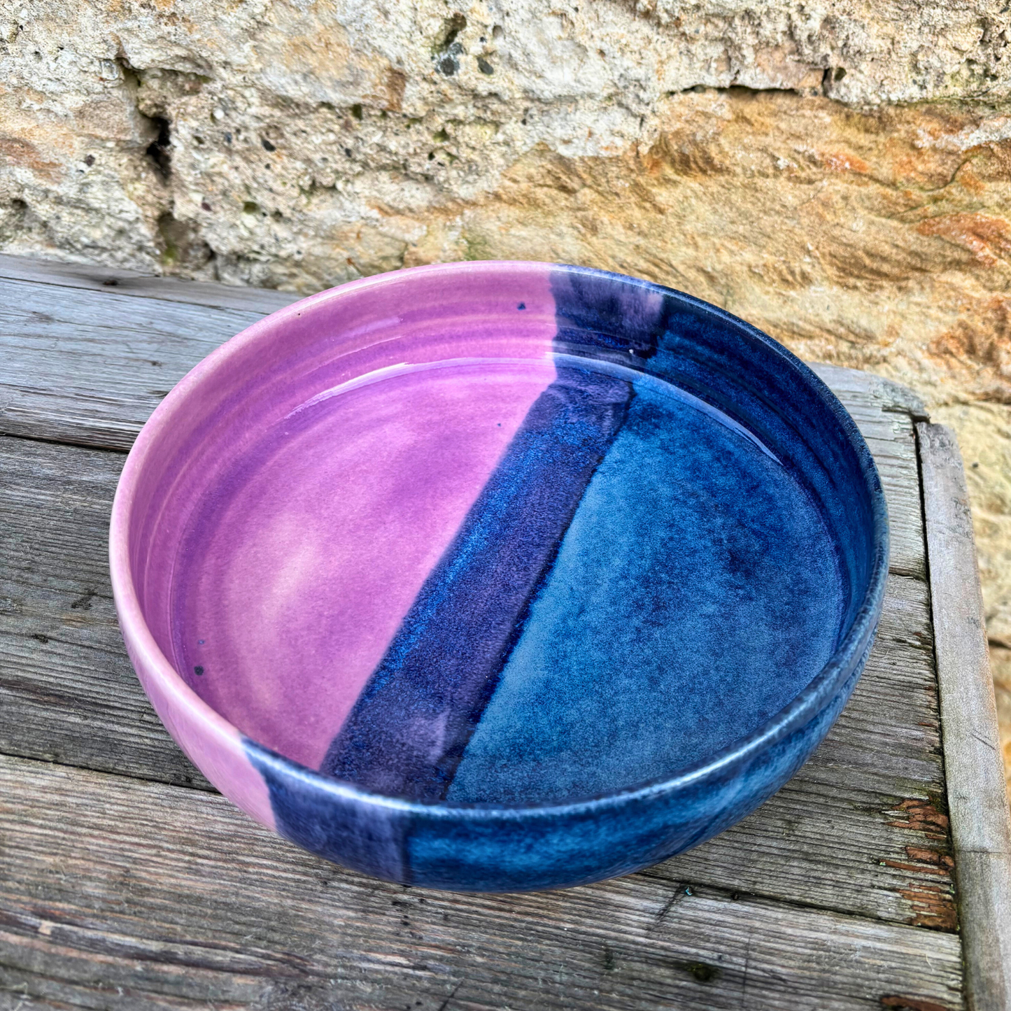 Ceramic bowl with pink and blue gradient on a wooden surface with stone wall background