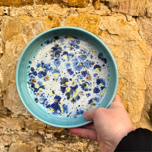 Hand holding a blue ceramic bowl with floral pattern against a stone wall.