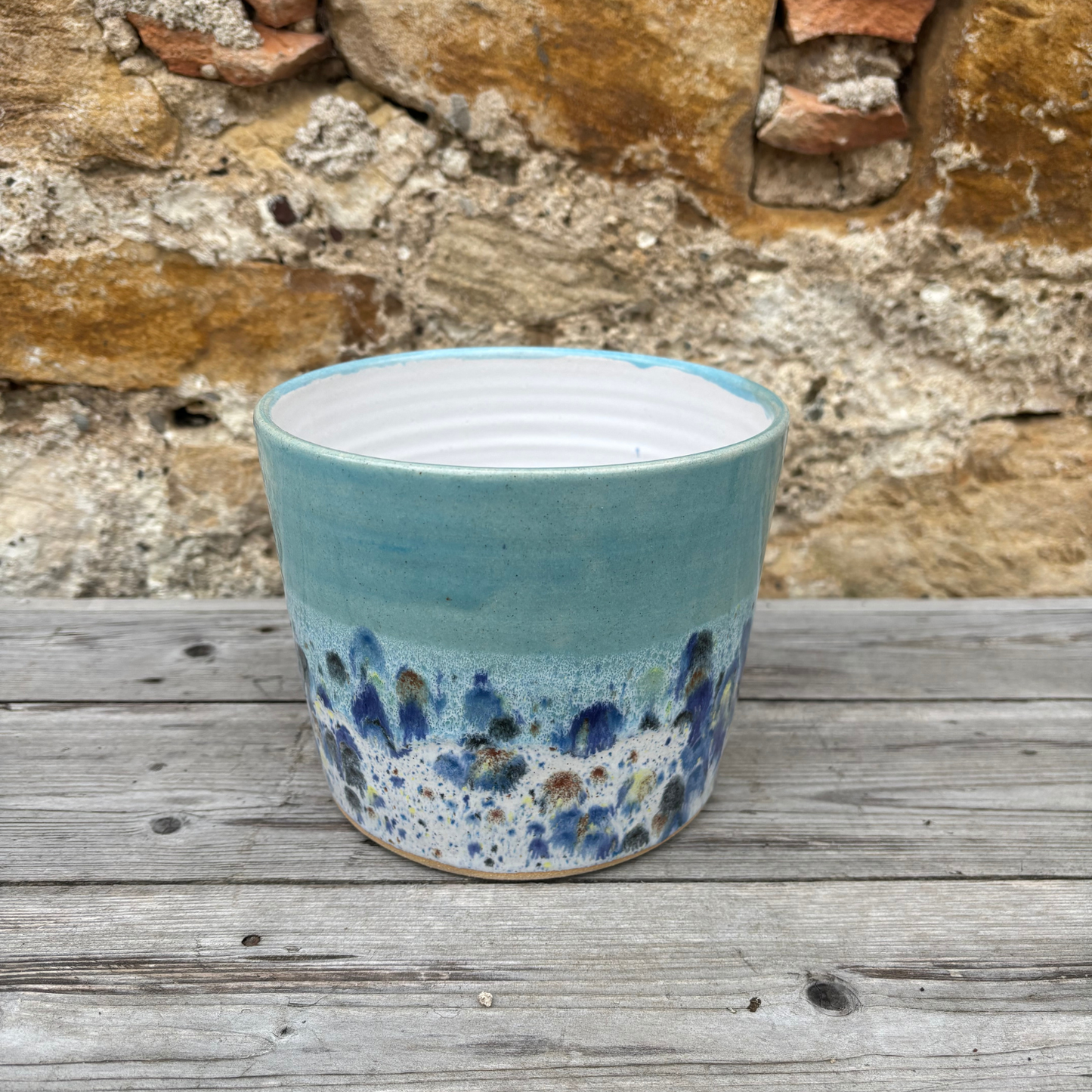 Blue ceramic pot with speckled design on a wooden surface with stone wall background