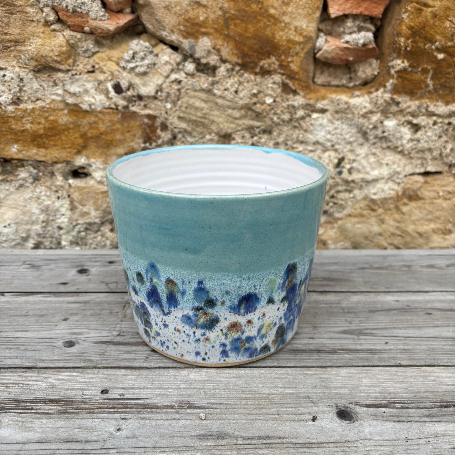 Blue ceramic pot with speckled design on a wooden surface with stone wall background