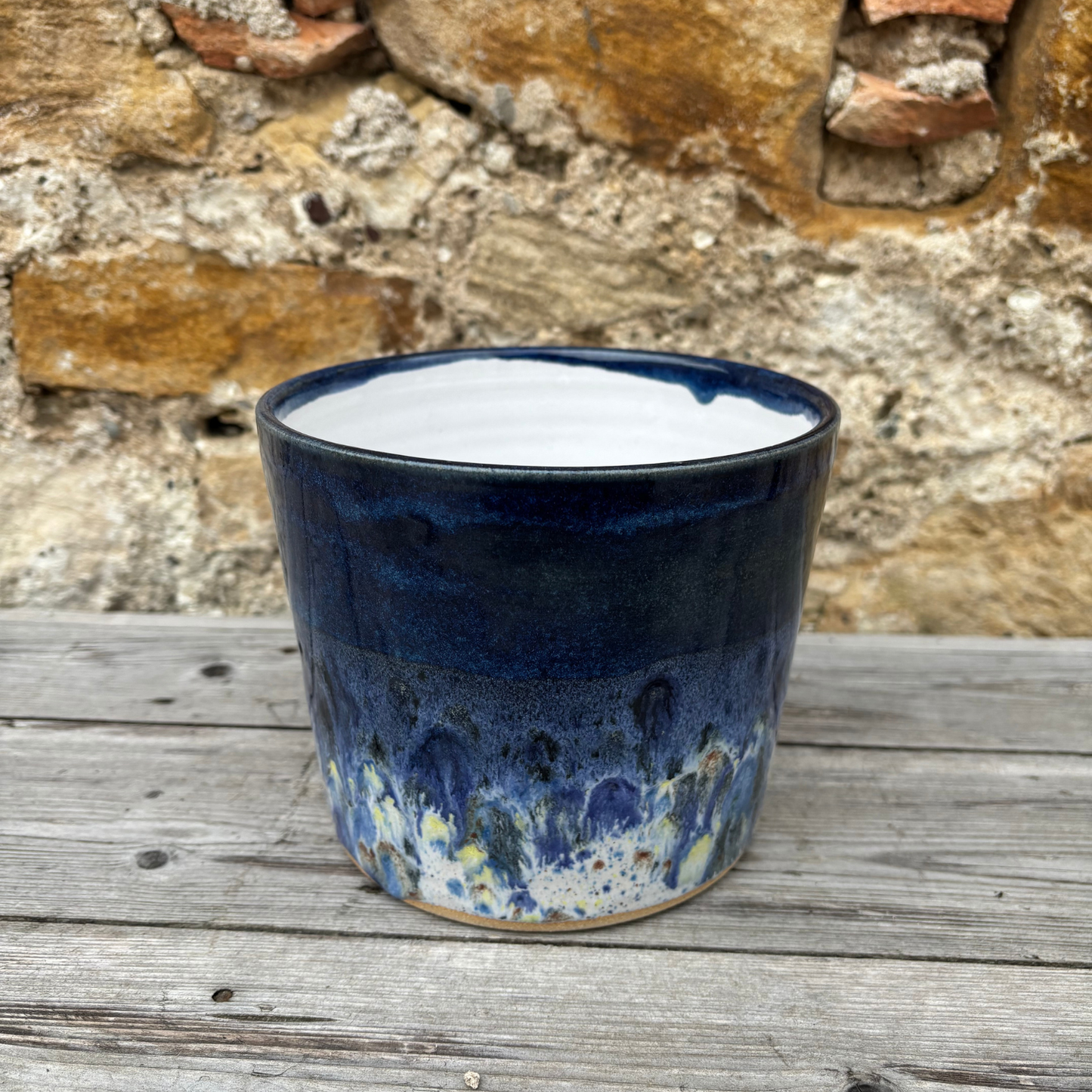 Blue ceramic pot on a wooden surface with a stone wall background