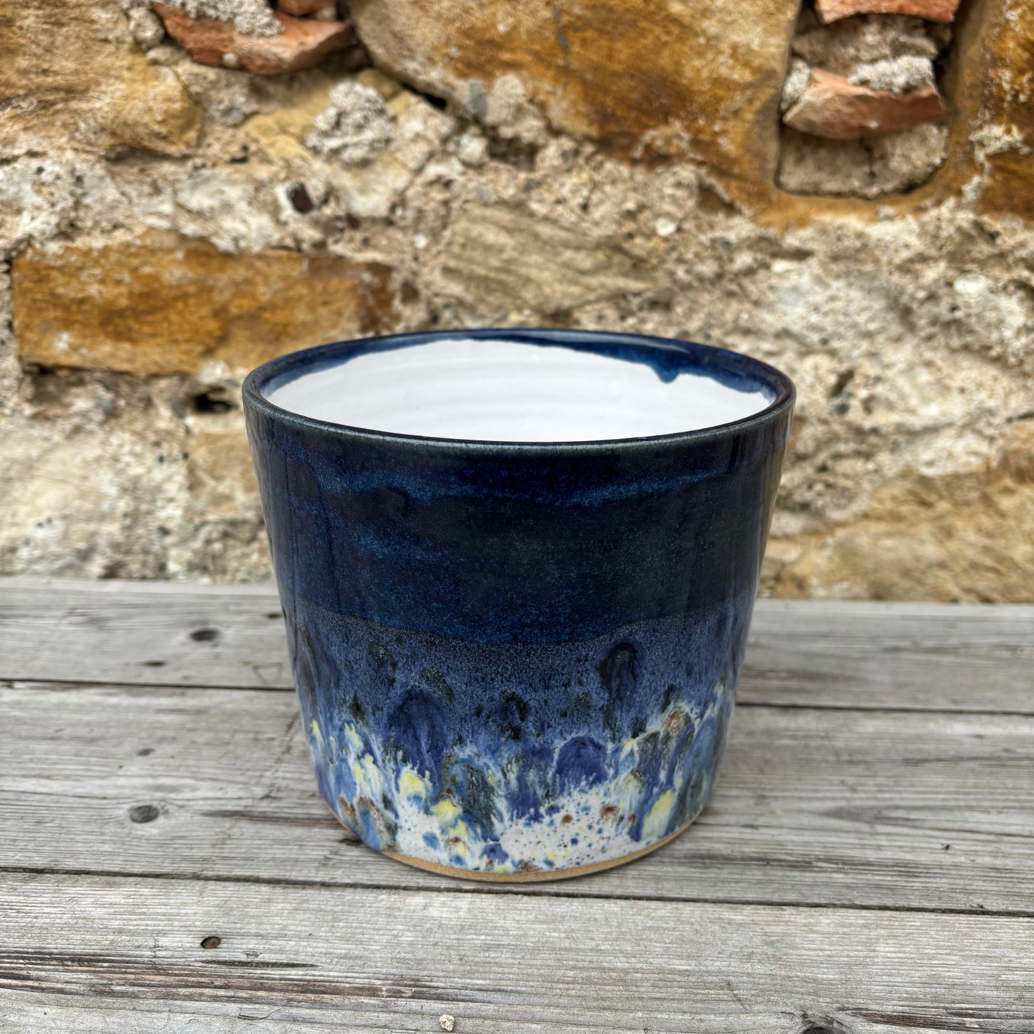 Blue ceramic pot on a wooden surface with a stone wall background