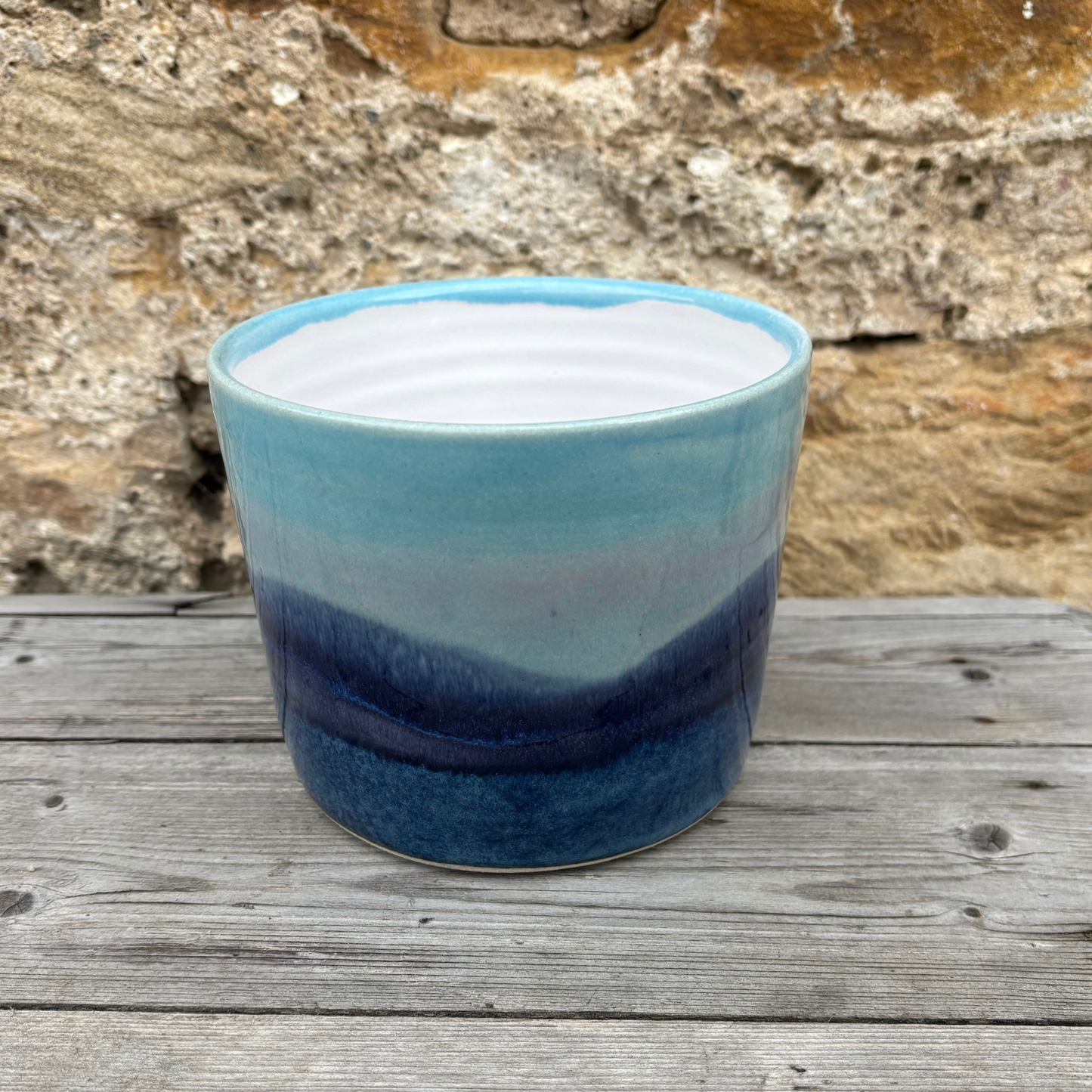 Blue ceramic pot with a textured surface on a wooden surface with a stone wall background