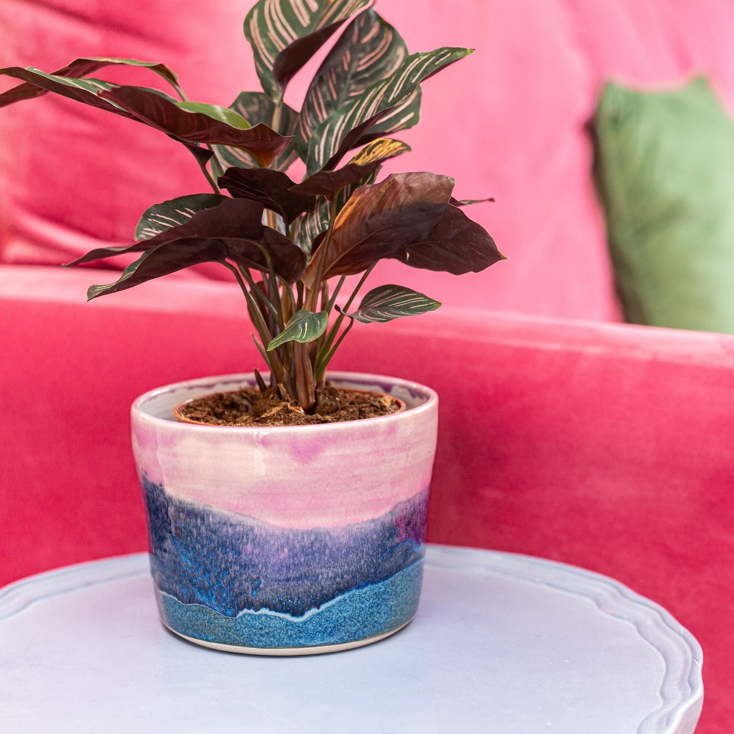 Ella Fletcher Designs Handmade Ceramic Pot in Pink Landscape Design on a side table with a plant