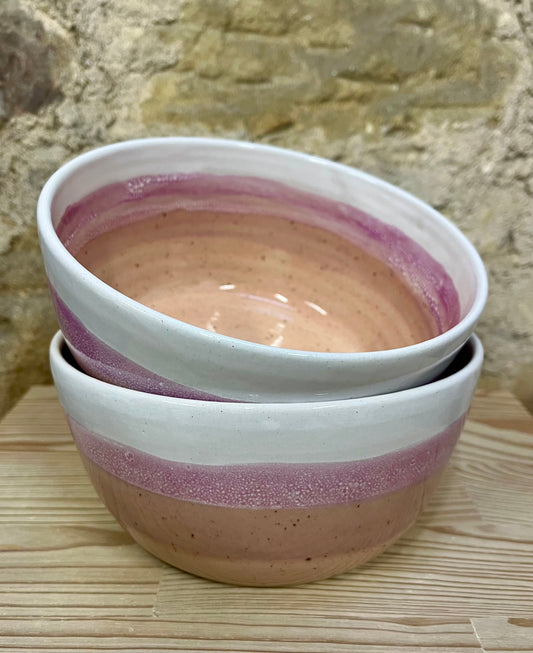Two stacked ceramic bowls with a pink interior and exterior rim against a stone wall background.